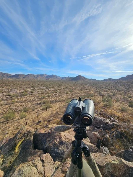Binoculars on a tripod in a desert landscape with mountains and a blue sky in the background.