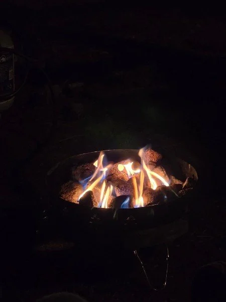 A small outdoor fire pit with burning logs and flames in the dark night.