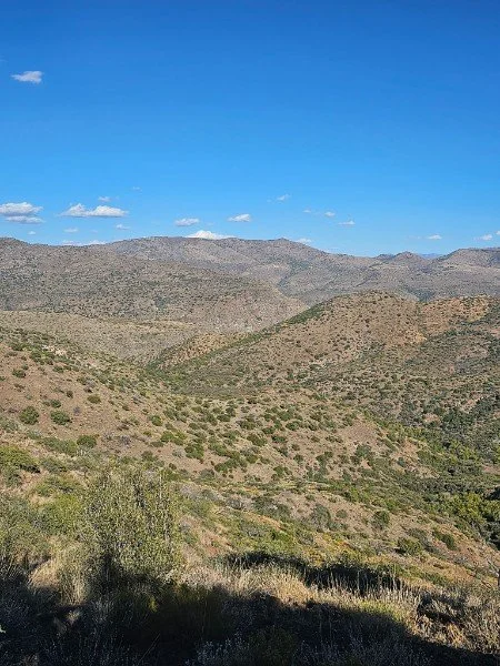 Scenic view of rolling hills and mountains under a bright blue sky with a few scattered clouds.