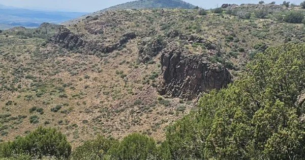 A landscape of rolling hills with sparse vegetation and rocky cliffs, with a distant mountain range in the background.