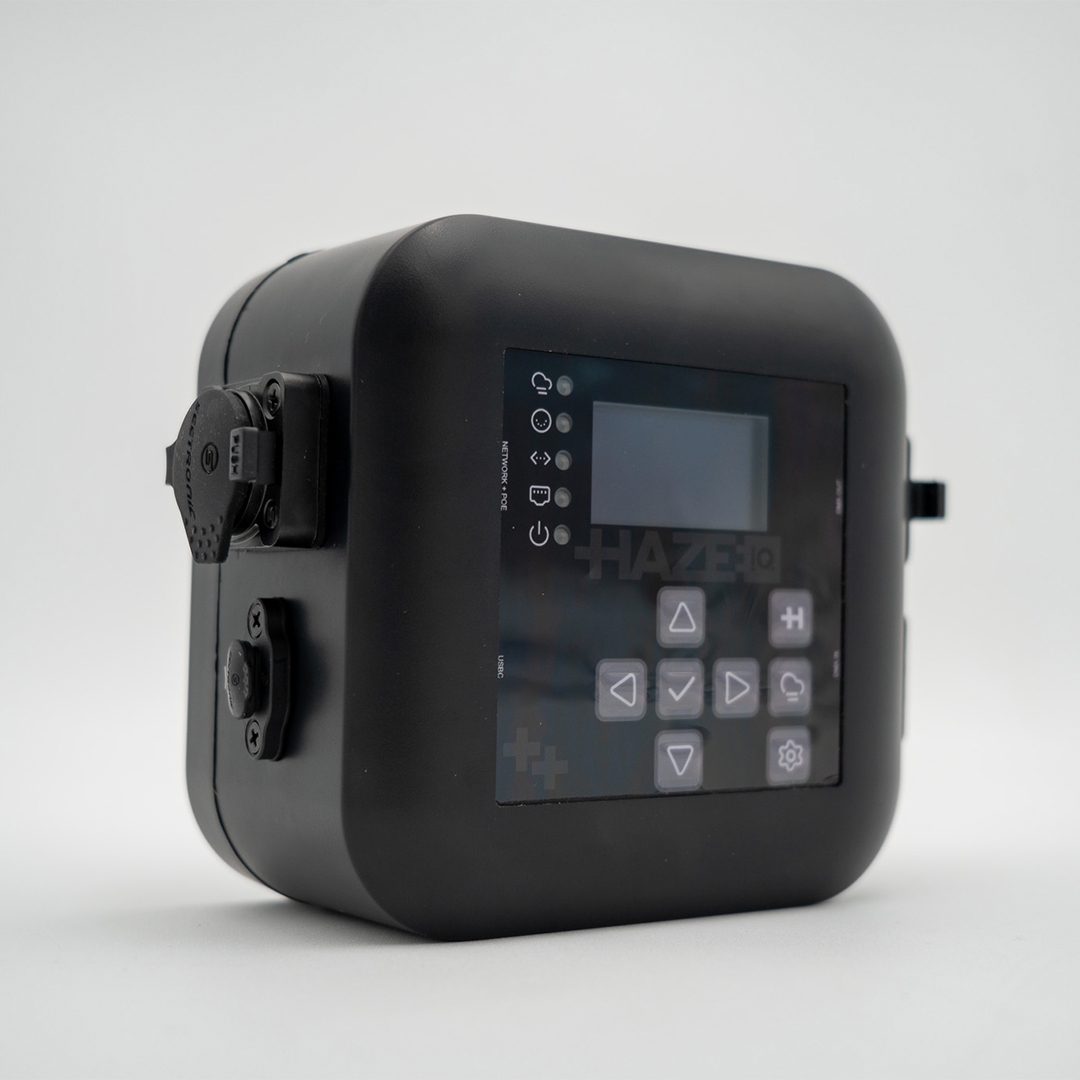 A HazeIQ control device with a digital screen and multiple buttons, resting on a white surface.
