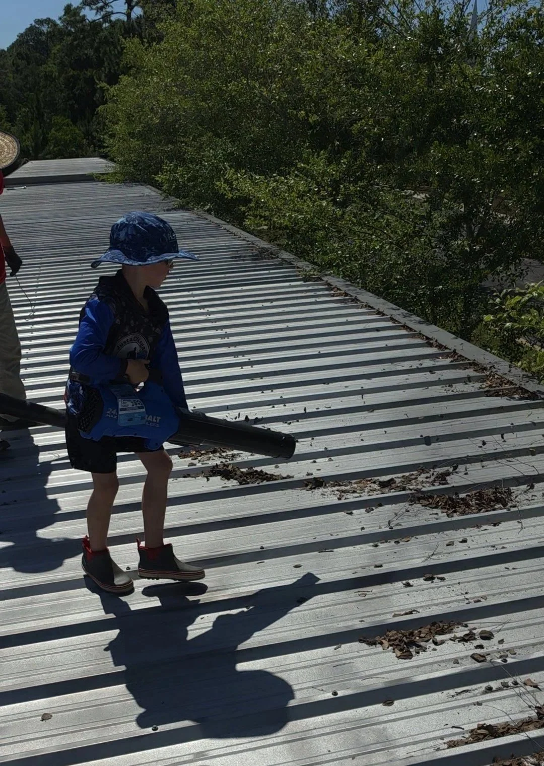 Professional gutter cleaning and debris removal from a metal roof to prevent residential water damage.