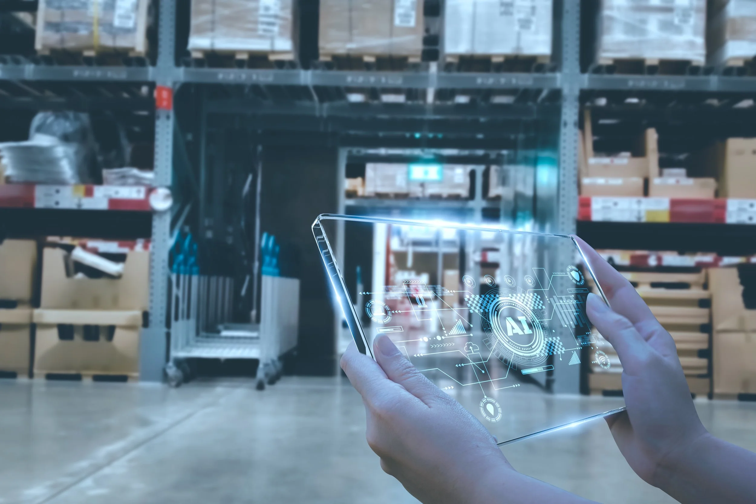 Person holding a transparent tablet with holographic AI and technology graphics, in a warehouse with shelves of boxed items.