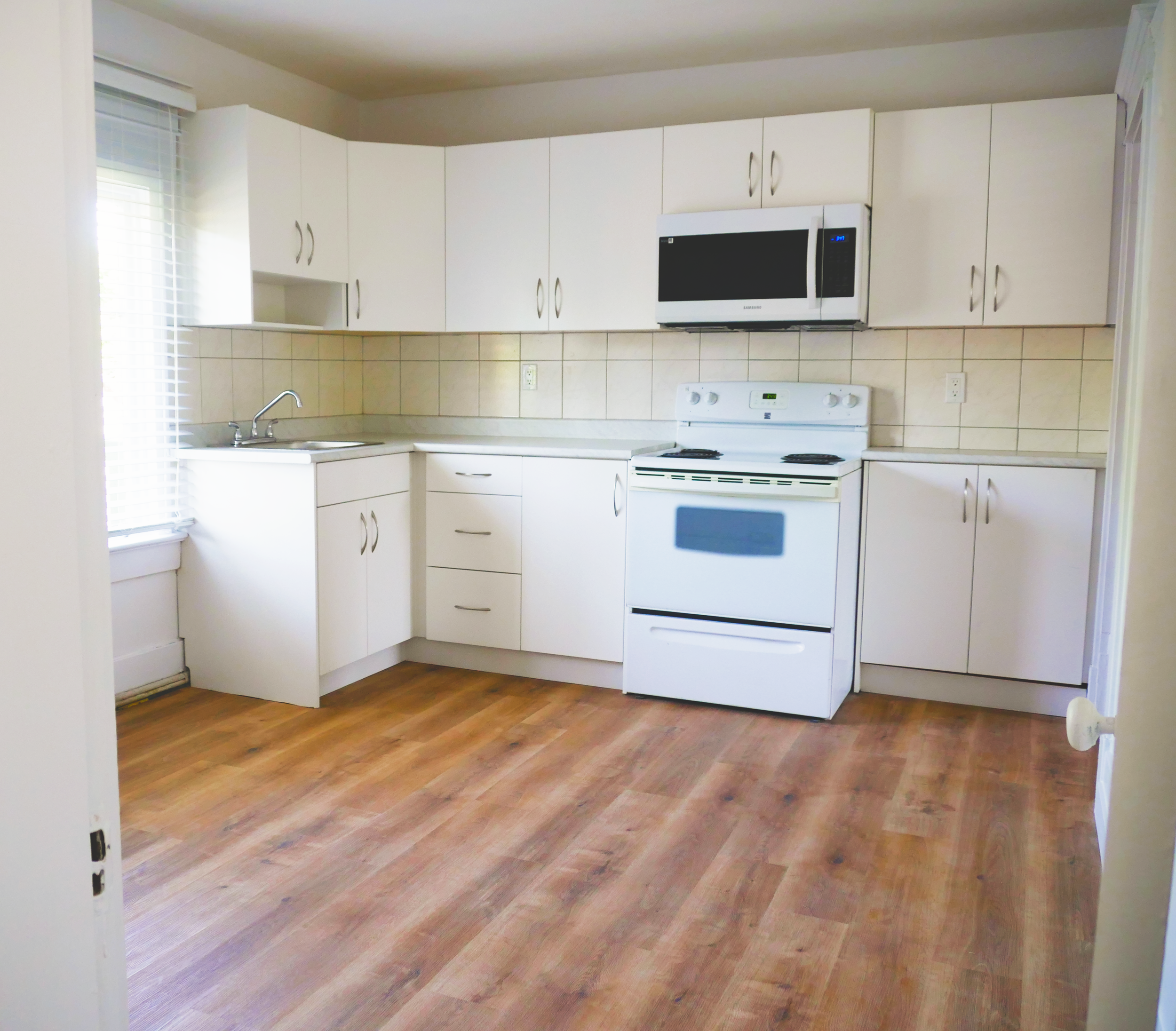 A kitchen with white cabinets, a stove, a microwave, a sink, and wood flooring.