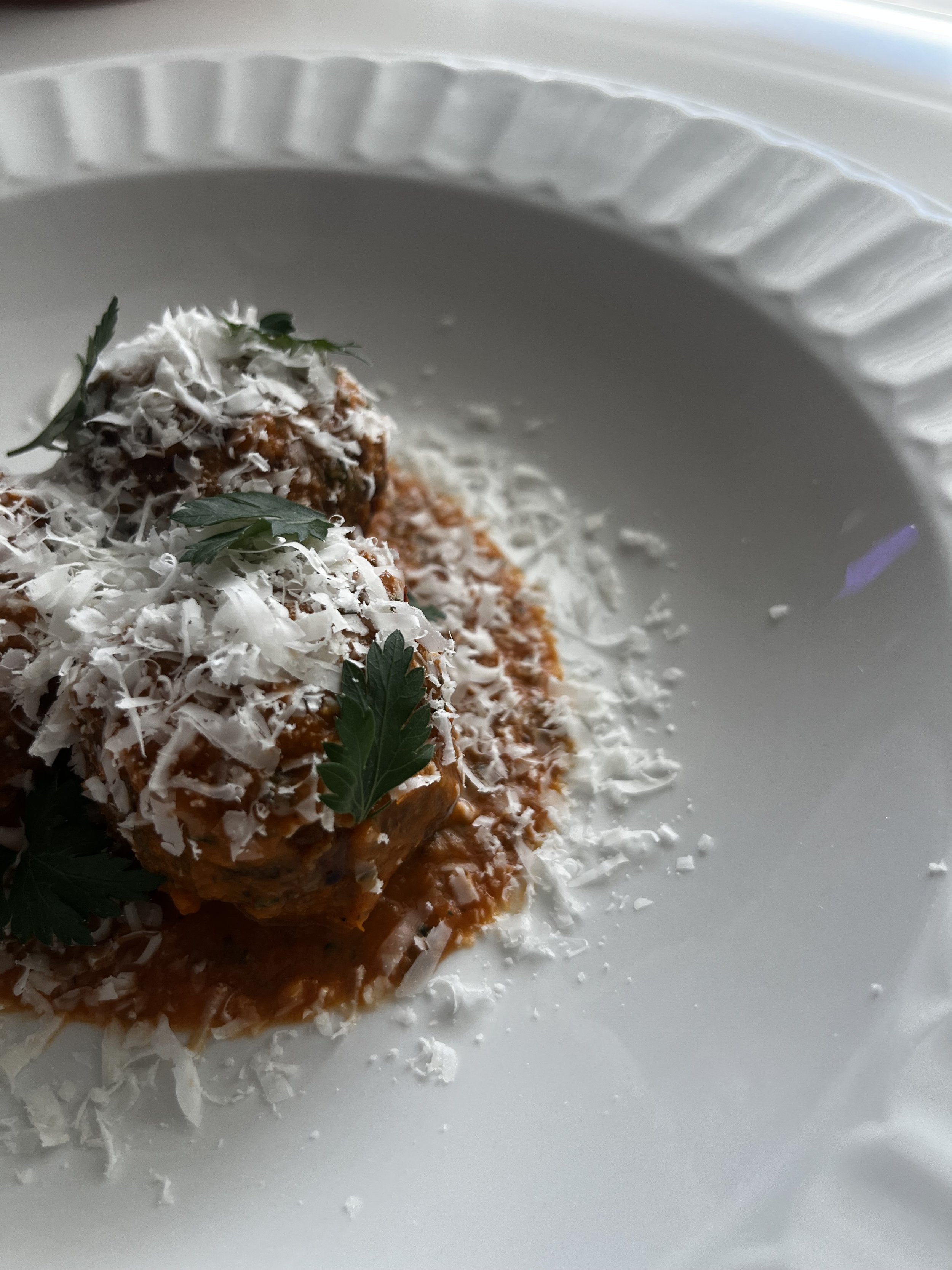 Meatloaf topped with shredded cheese and garnished with parsley on a white plate.
