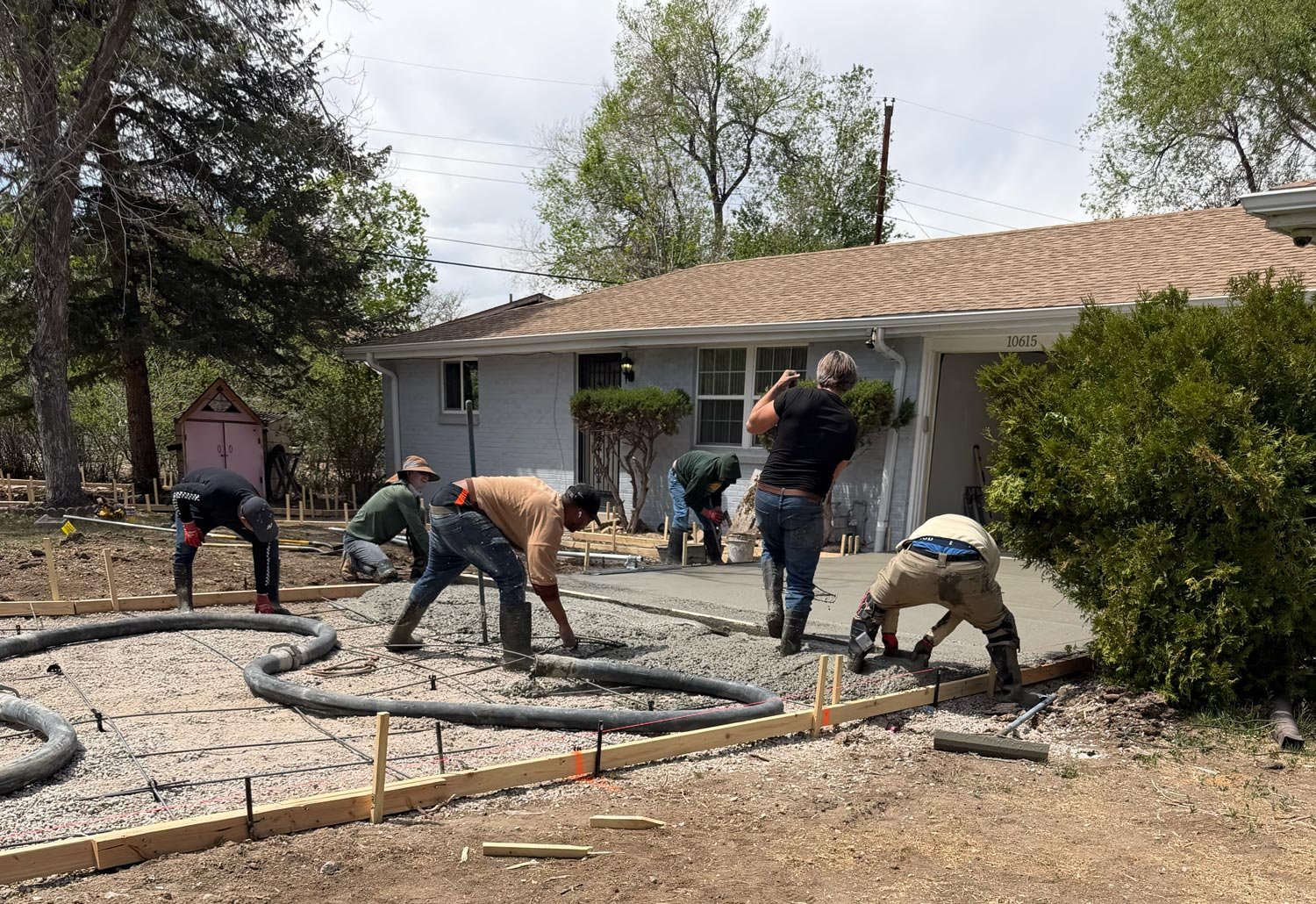 Team of construction workers pouring and leveling concrete in a residential driveway during daytime.