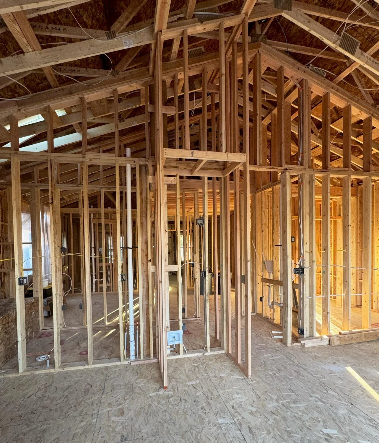 Interior view of a house under construction with exposed wooden framing, including walls, doorways, and ceiling trusses.