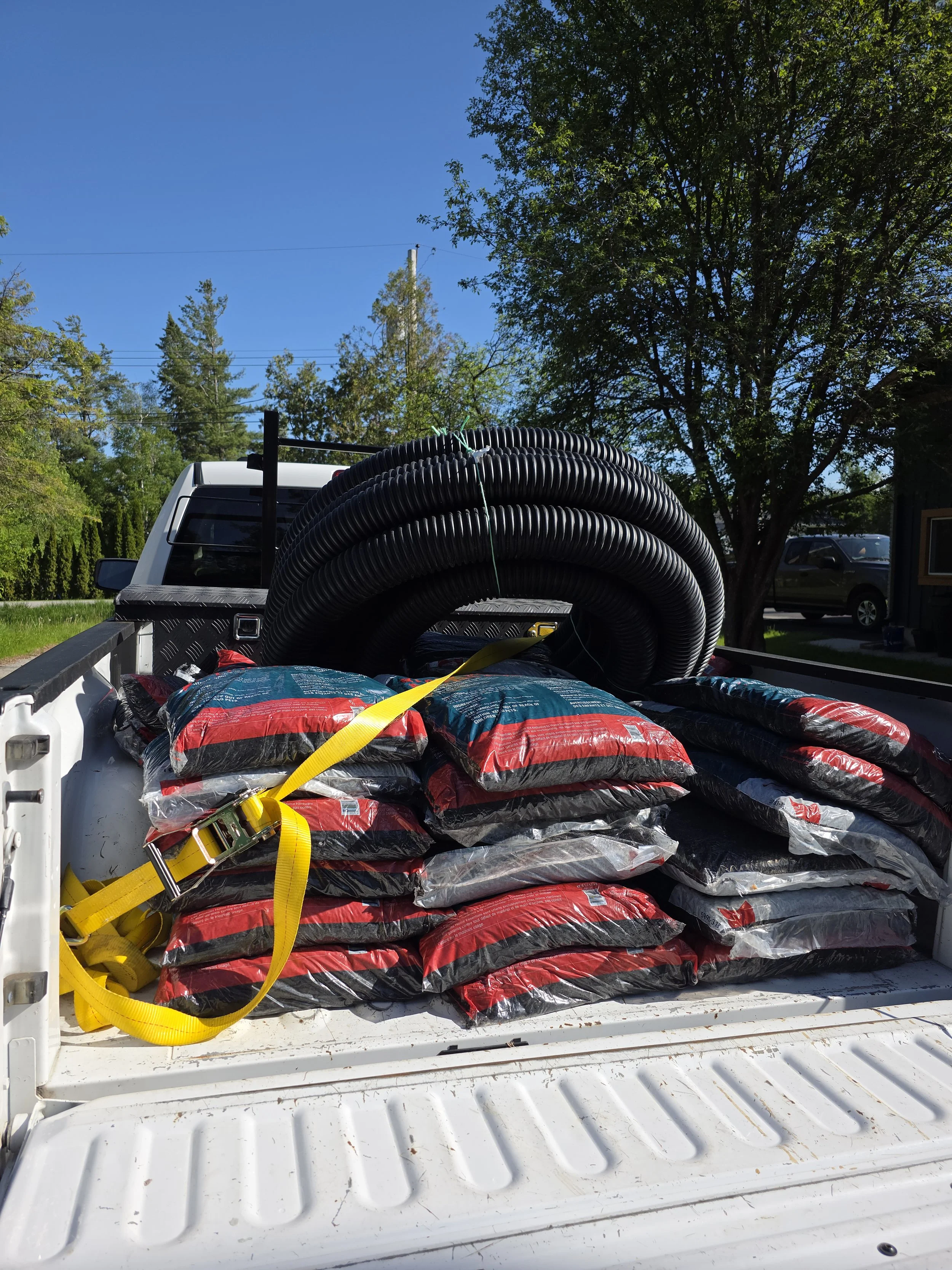 Drainage materials loaded in a work truck including corrugated drain pipe and aggregate for residential drainage and water management projects.