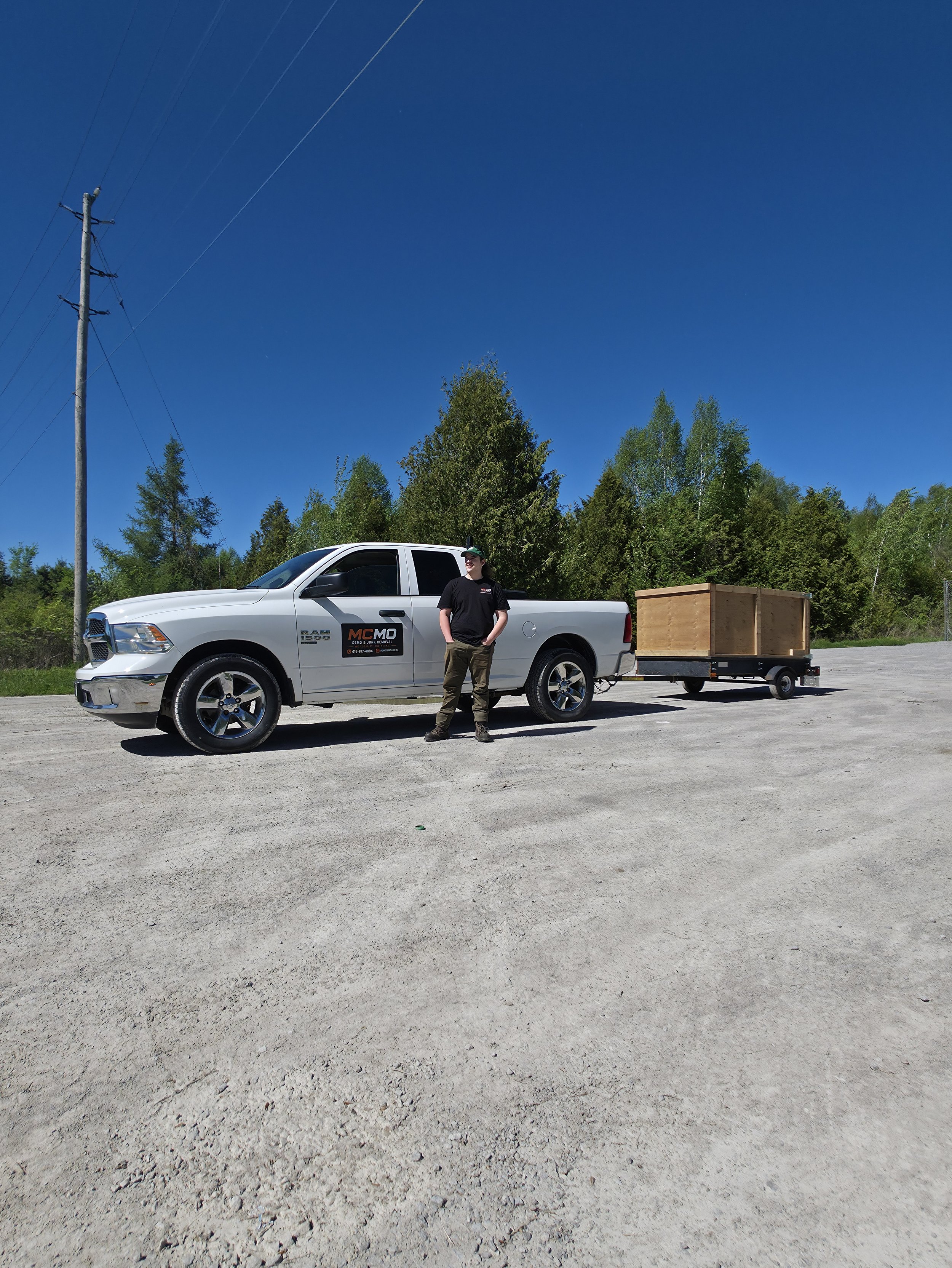 Owner of McMo Demo & Junk Removal standing beside a branded white Ram 1500 pickup truck and utility trailer in Georgina, Ontario.
