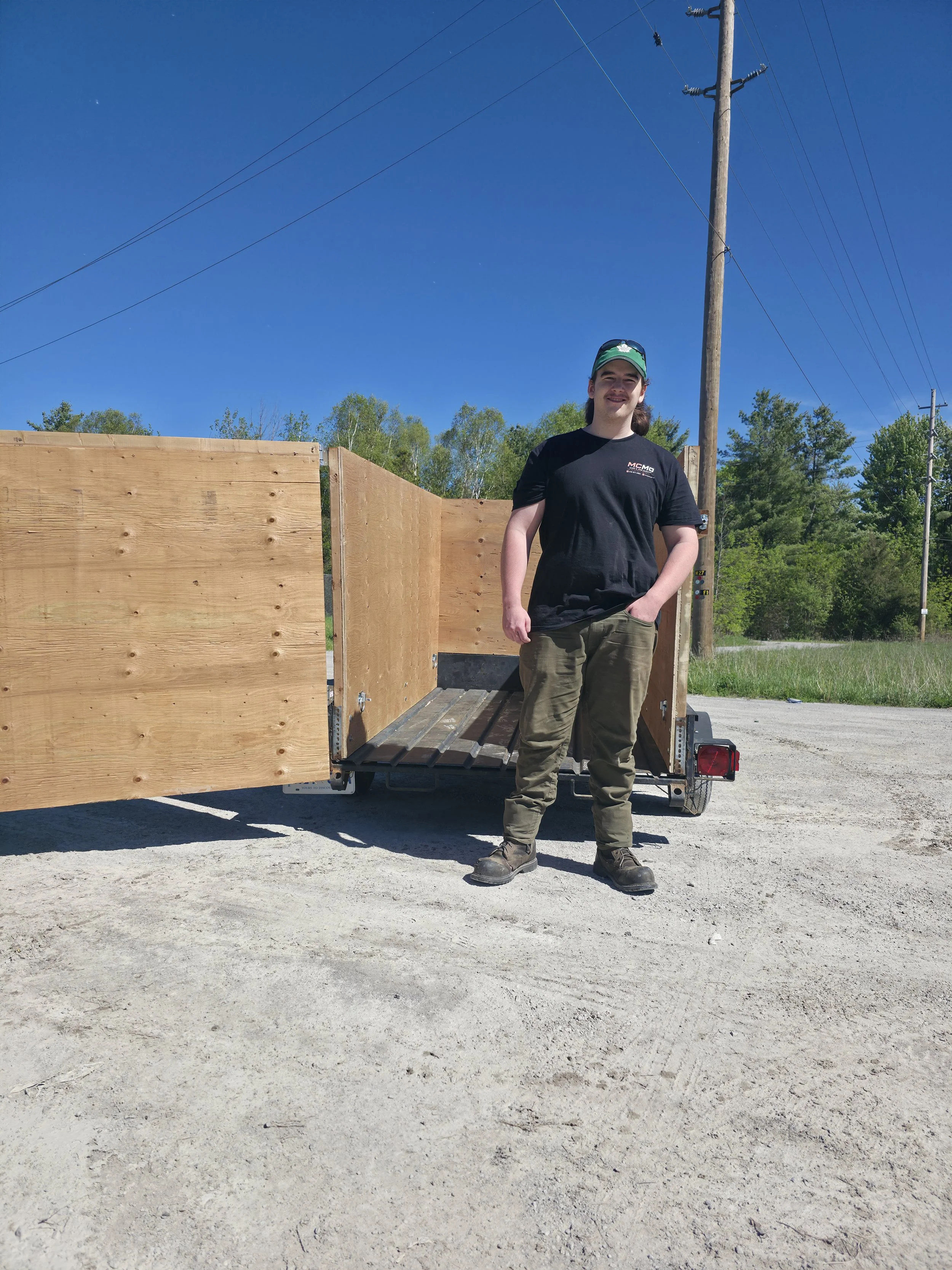 Owner-operator of McMo Demo & Junk Removal standing beside a utility trailer, providing demolition, junk removal, drainage, and handyman services throughout Georgina and surrounding communities.