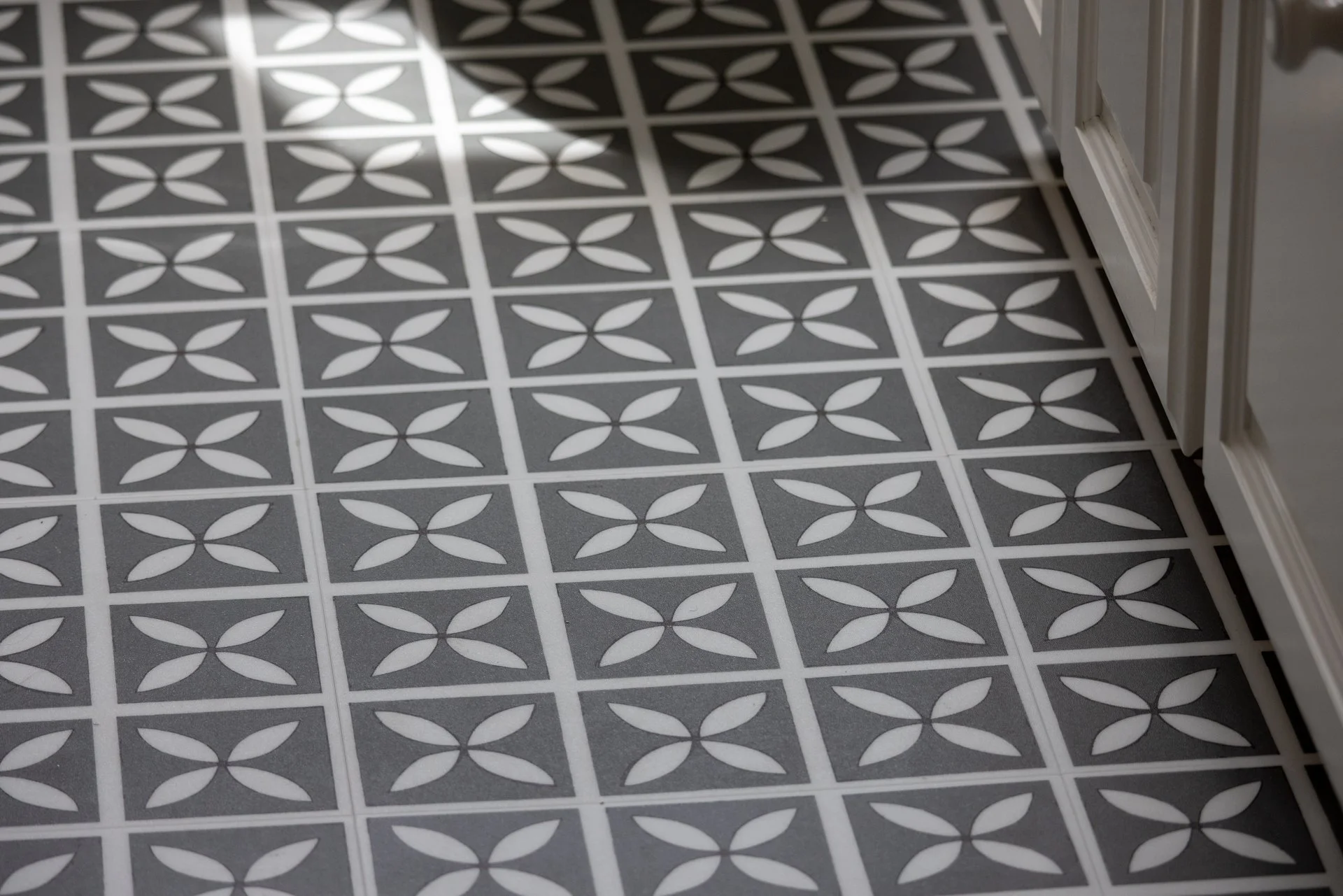 Patterned floor tiles with a geometric design of white leaf shapes on a gray background.