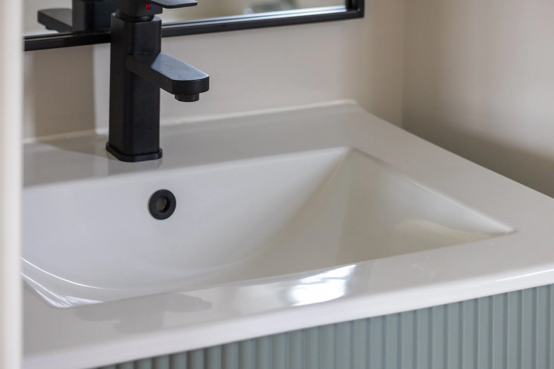 A white bathroom sink with a black faucet and a mirror above it.