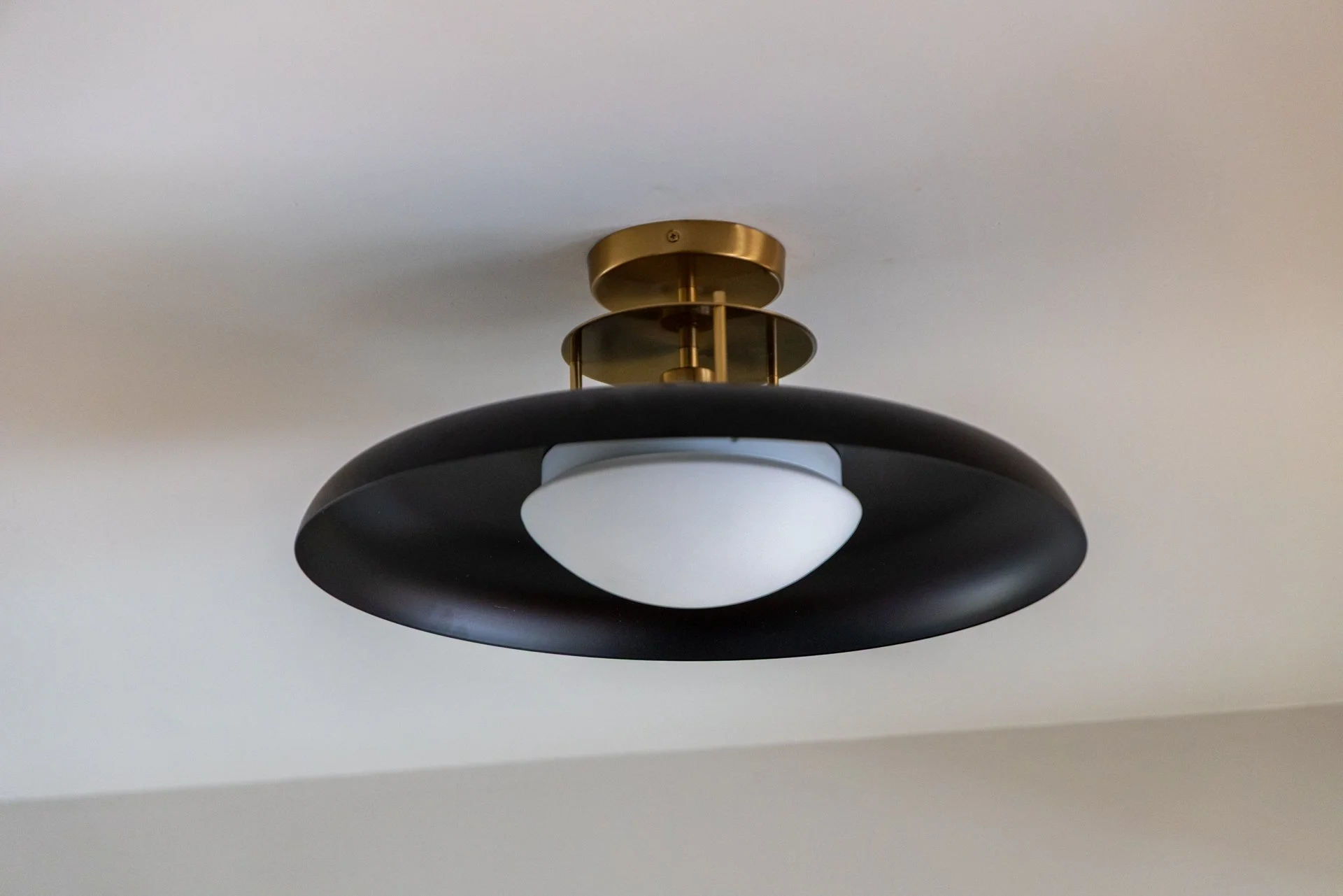 Ceiling light fixture with a black outer ring, a white inner diffuser, and brass components, mounted on a white ceiling.