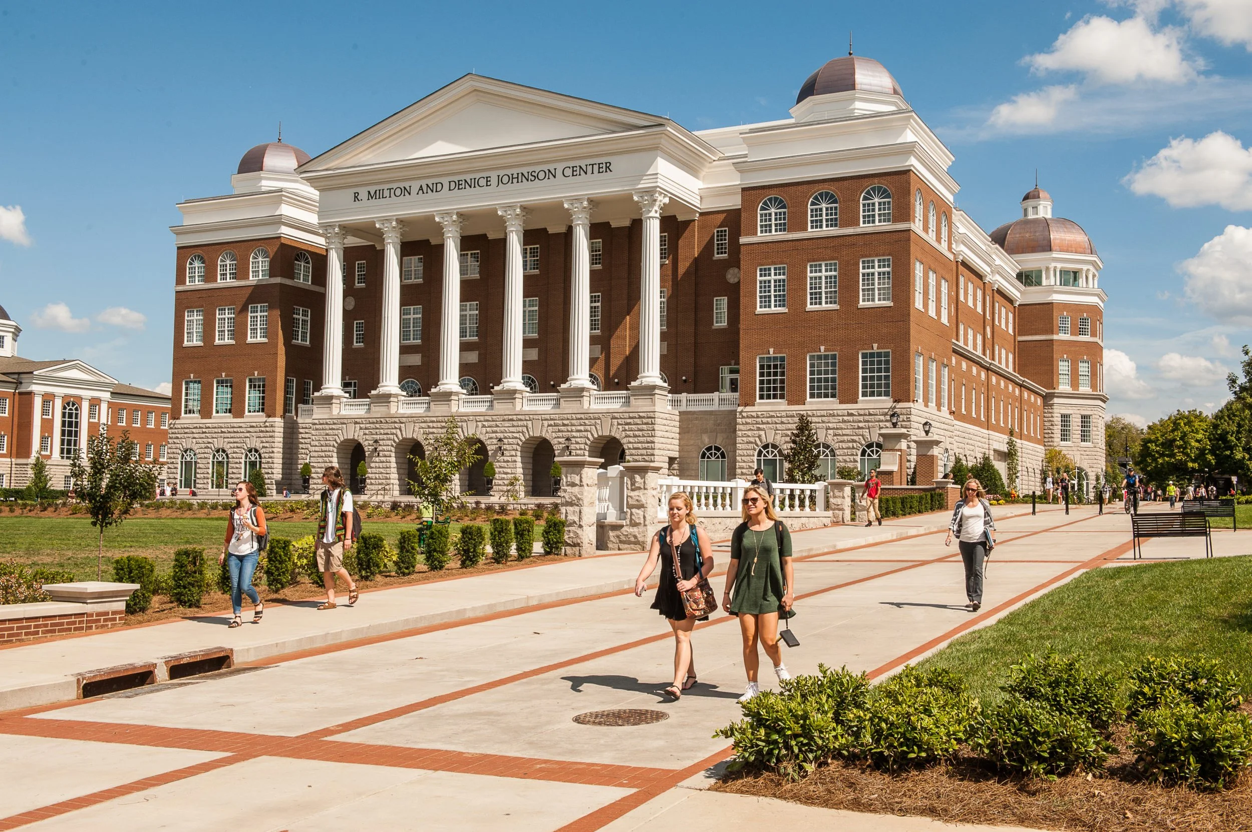 Students walking outside the R. Milton and Denice Johnson Center, a large red brick building with white columns and a prominent sign.