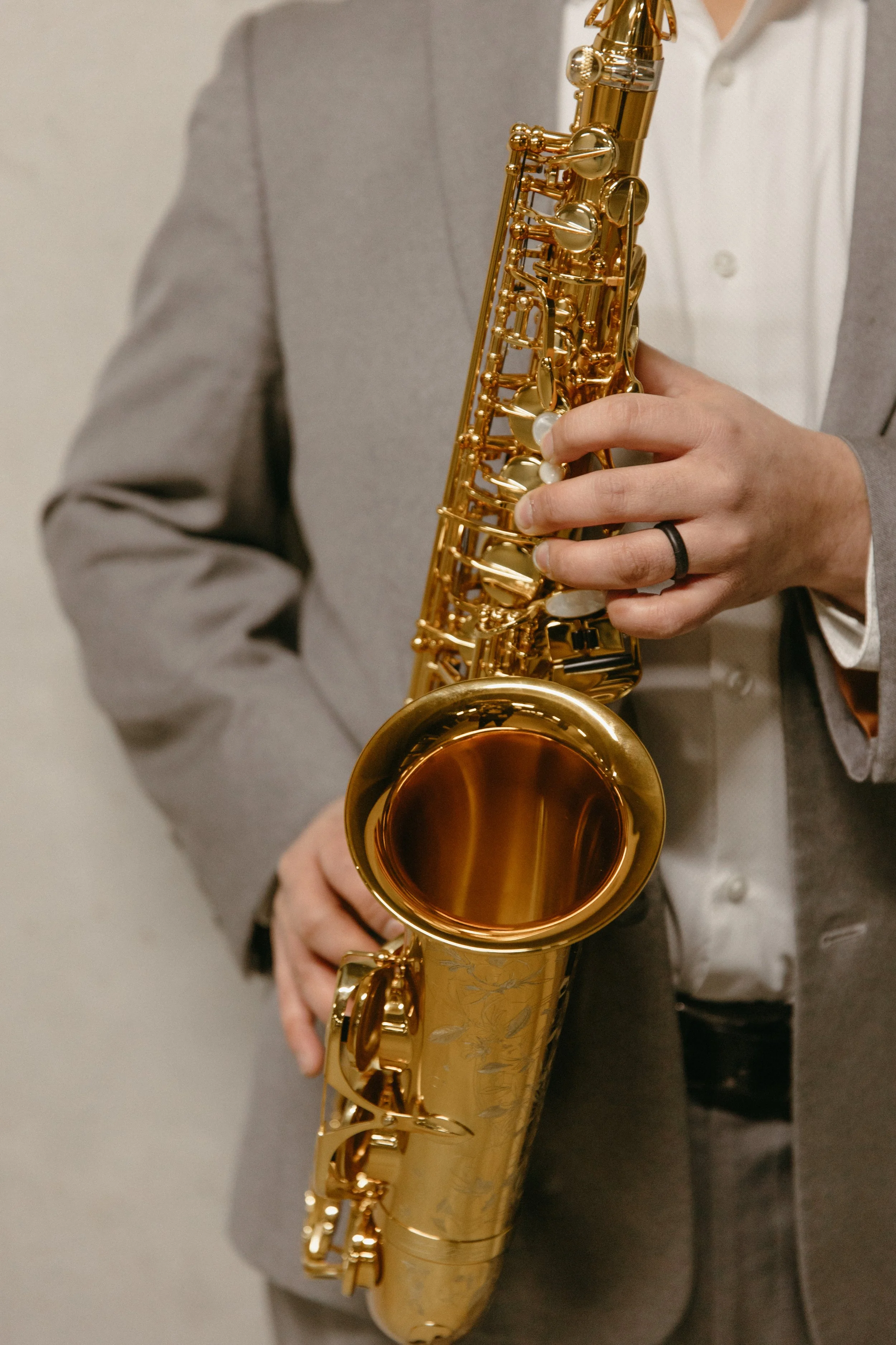 A person dressed in a gray blazer and white shirt holding a gold-colored saxophone.