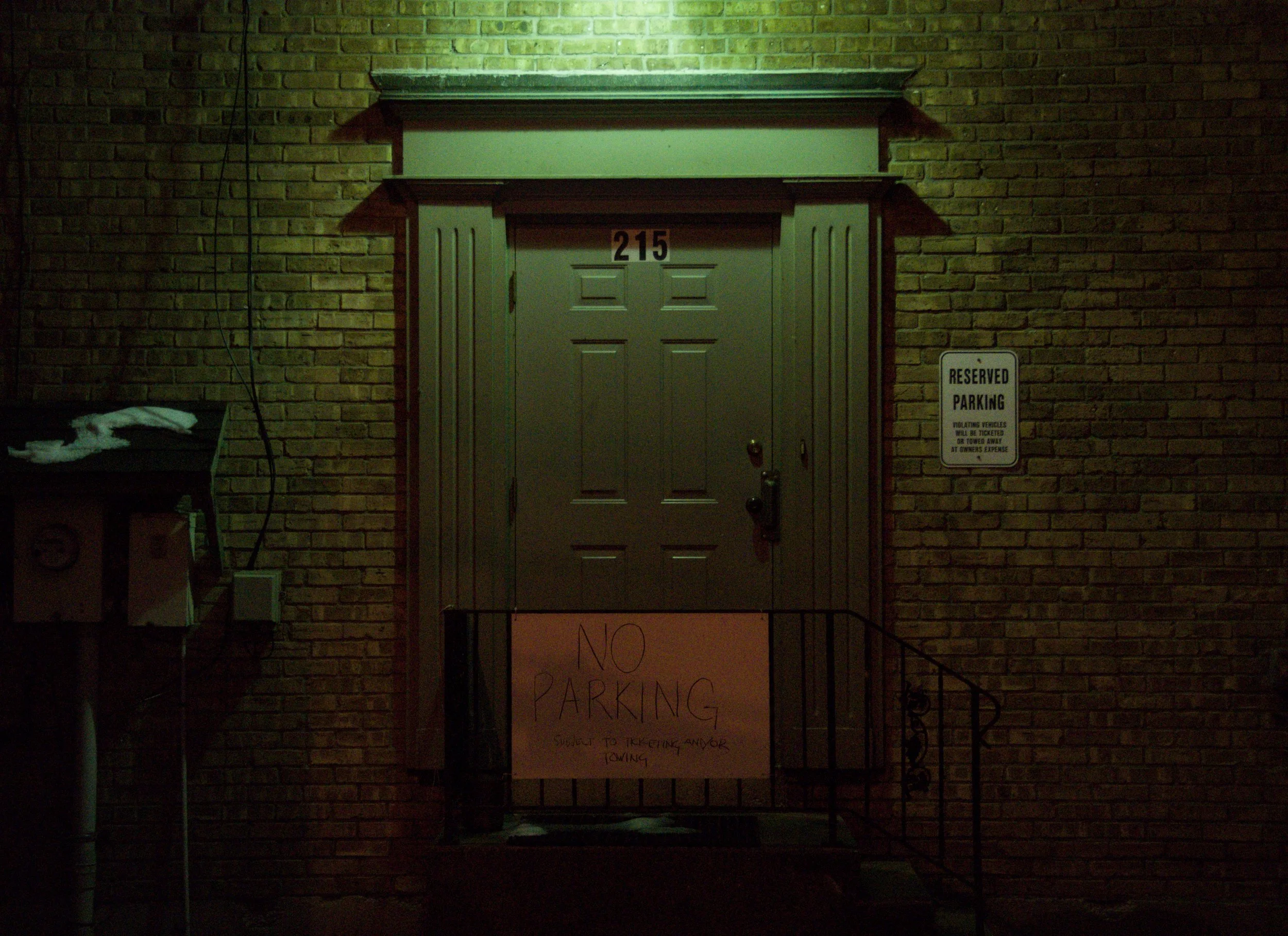 A headlight door at night with a no parking sign hanging on its guardrail.