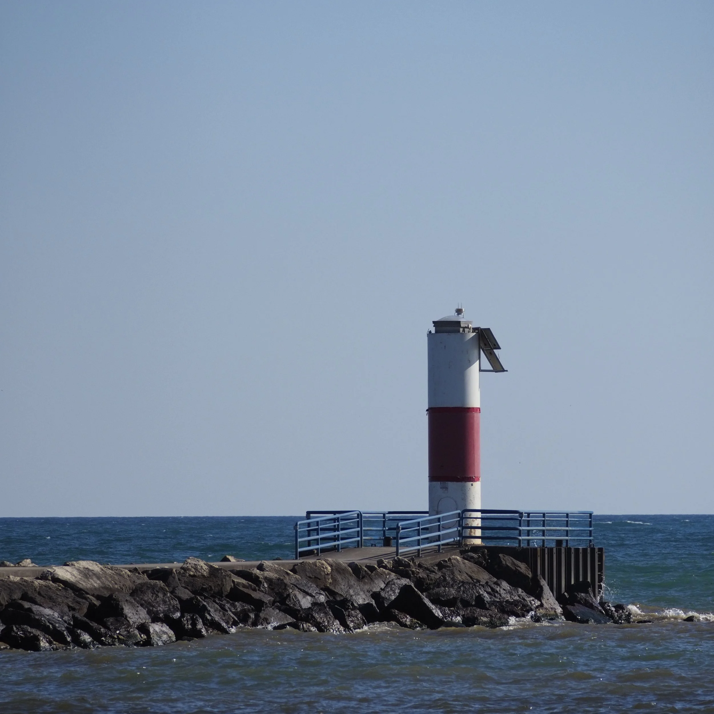 A lighthouse looking over a coast. A stone pier leads off frame.