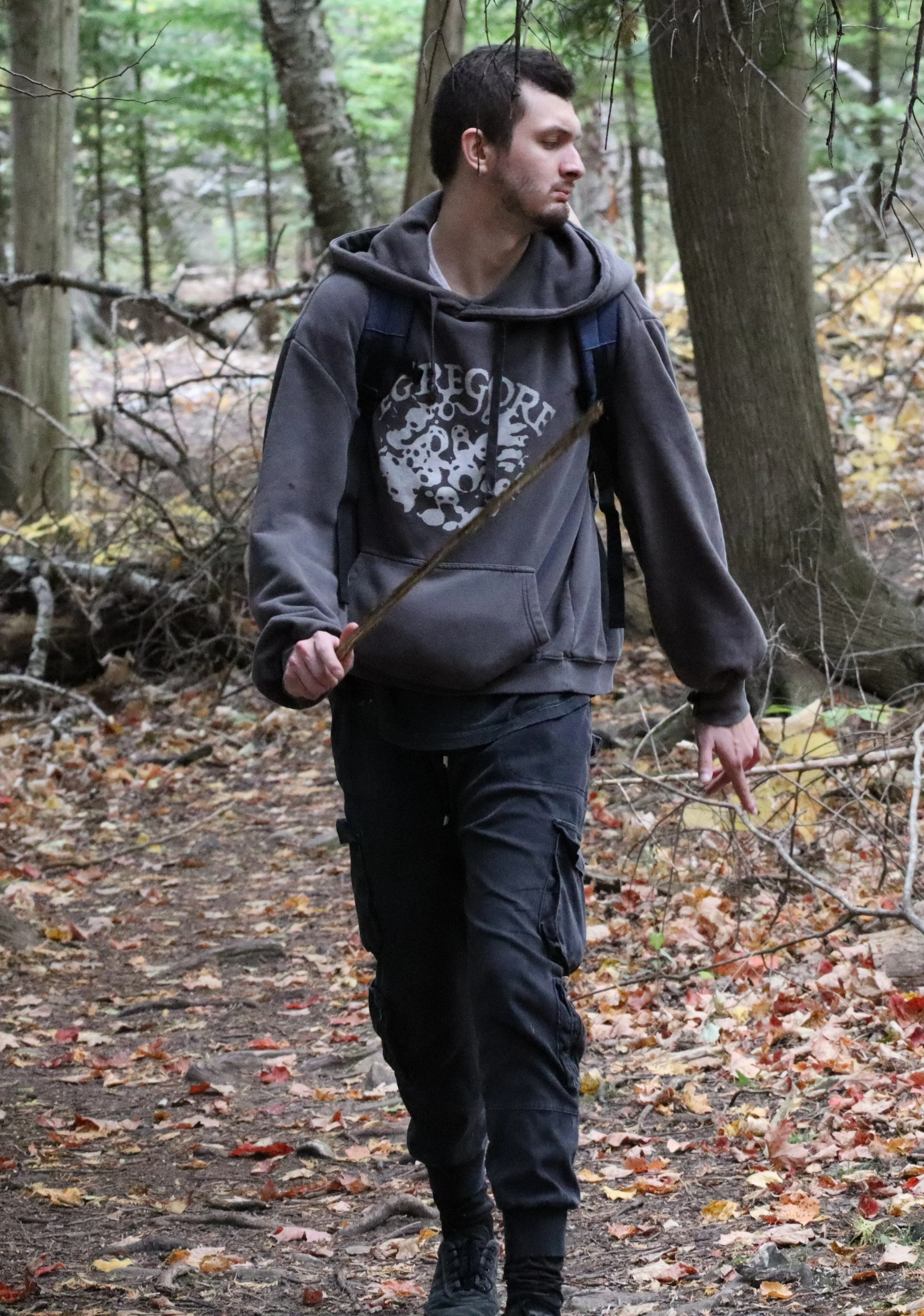 Me :) A man walking with stick in hand. Wearing a gray "egregore" hoodie with an oversized hood and some denim techwear joggers.