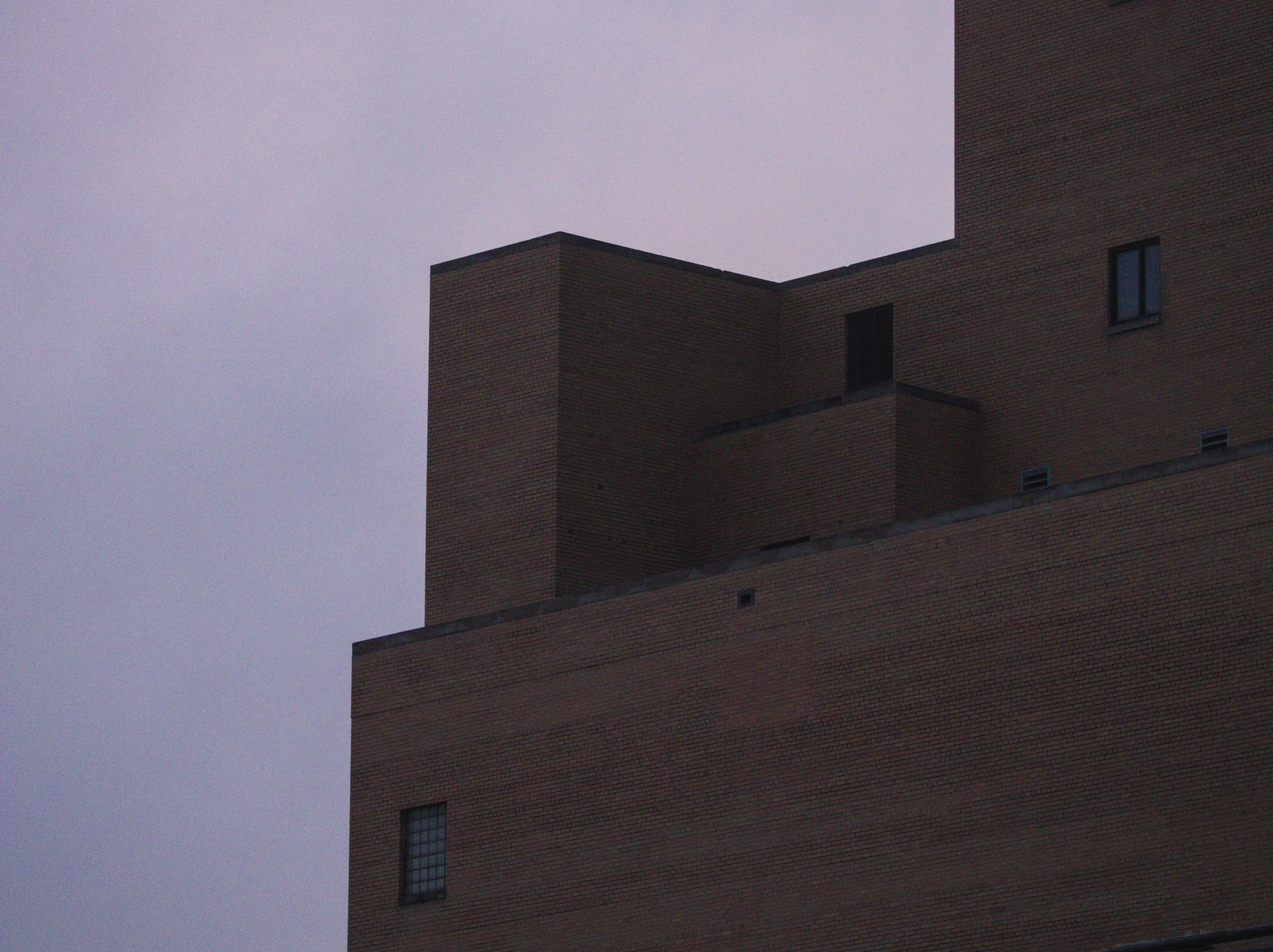 Geometrical rooftop contrasting a dusk sky. A single door stands on an upper ledge.