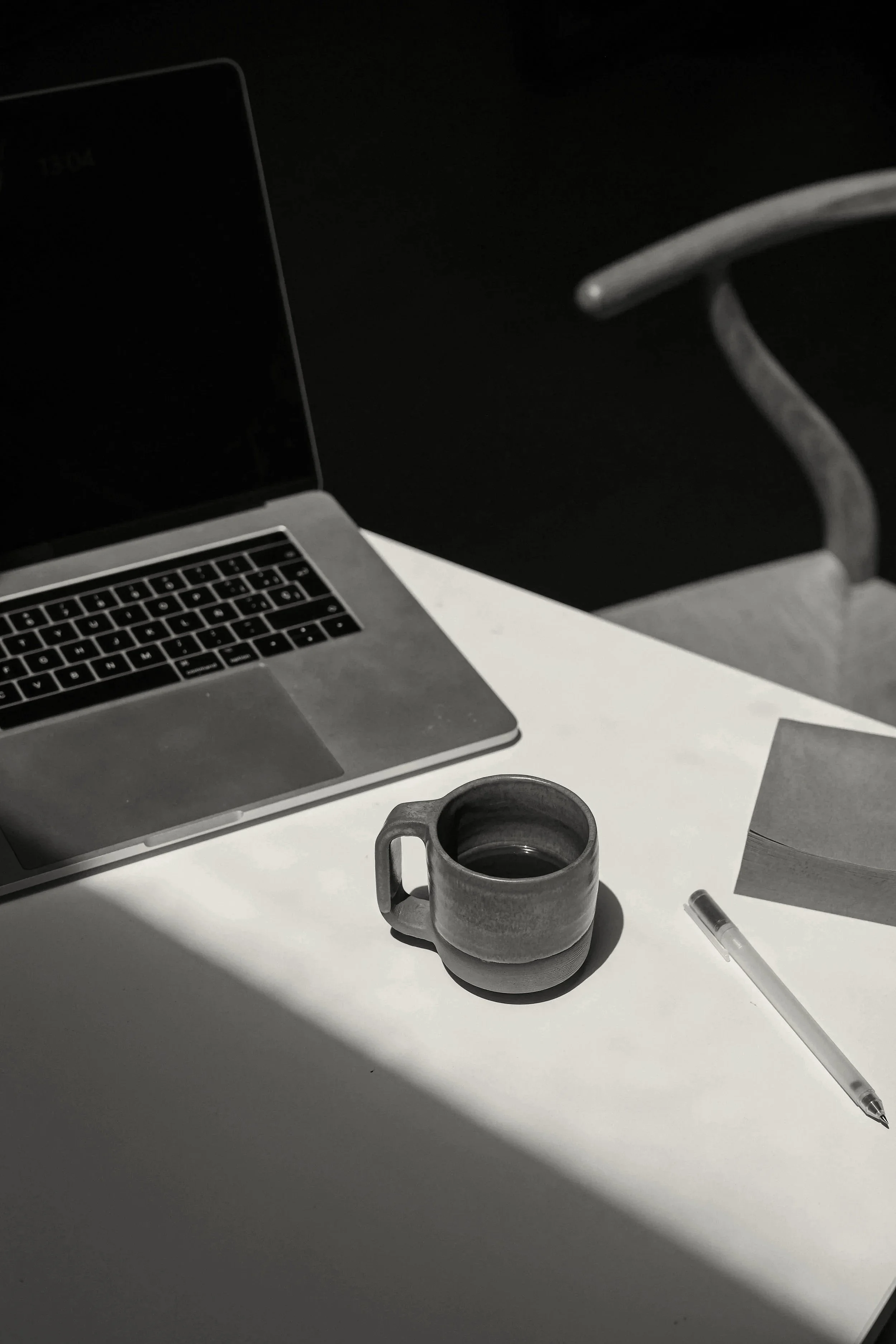 Desk with laptop, a cup of coffee, papers, and a pen, with a black background and white surface.