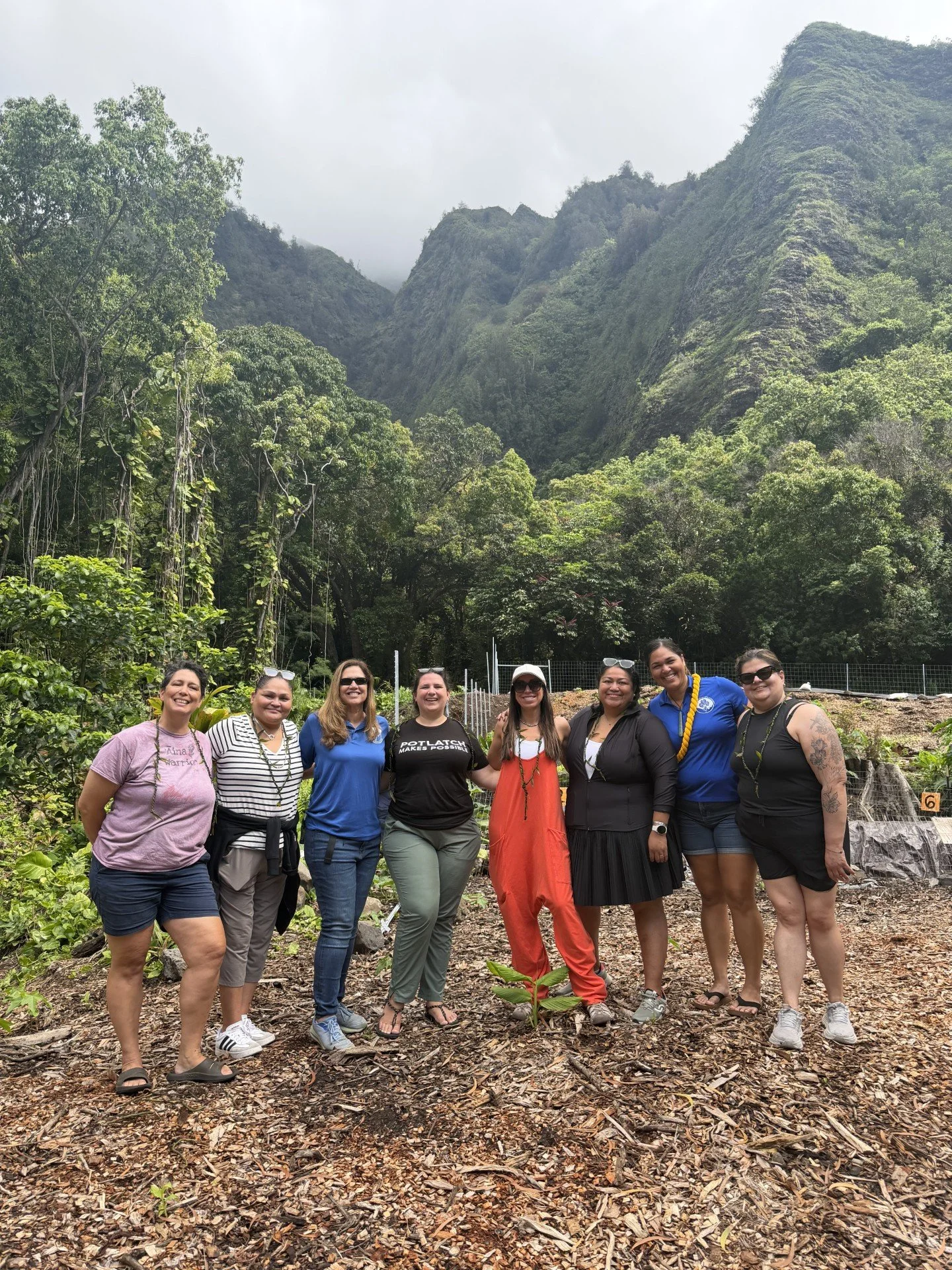 Group of eight women standing outdoors in a lush green mountainous area, smiling and posing for the photo.