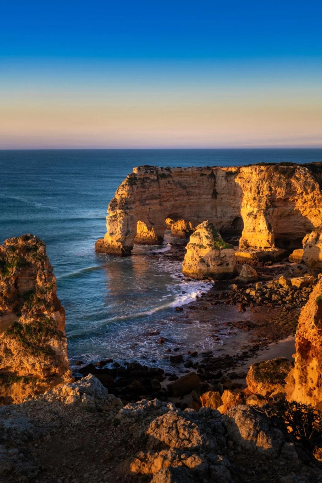 Sunset over the ocean with large, rocky cliffs and natural arches on the coastline.