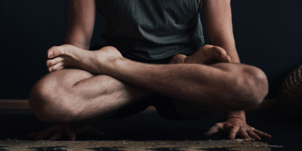 Person sitting cross-legged on a dark rug with arms resting on knees