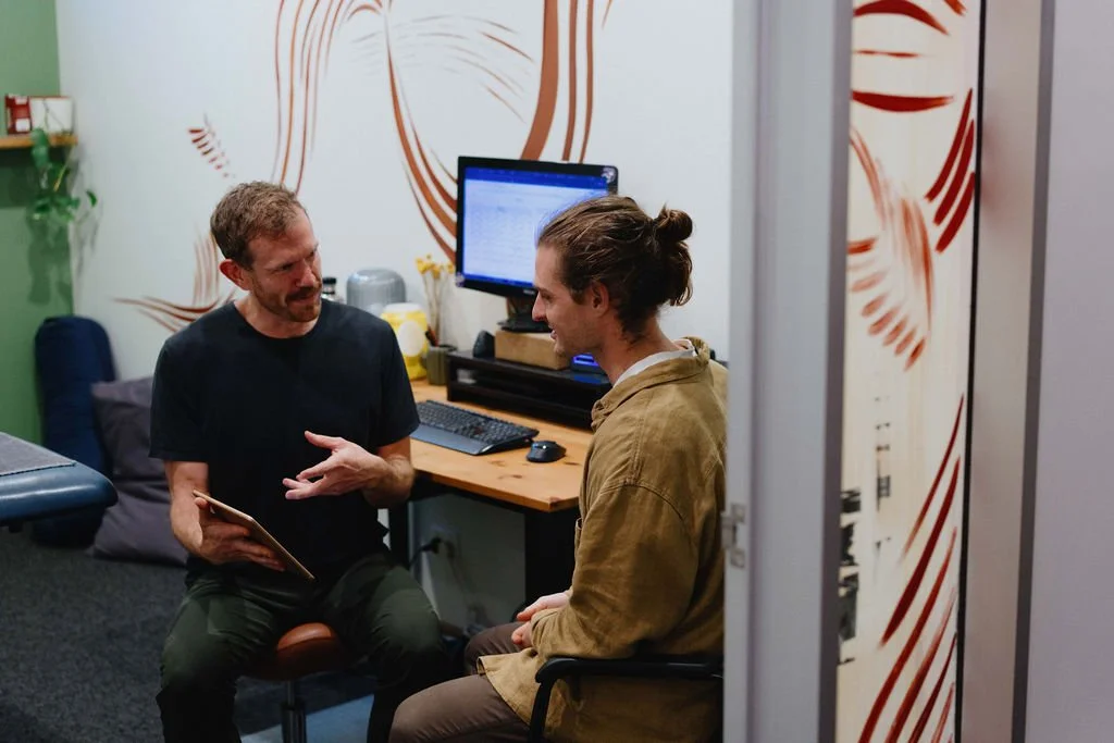 A physiotherapist is advising a client showing images on a tablet in a consultation room