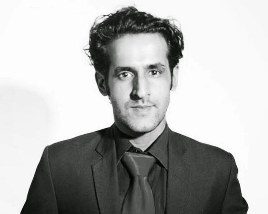 Man stands facing the camera in a dark suit in a black and white professional shot