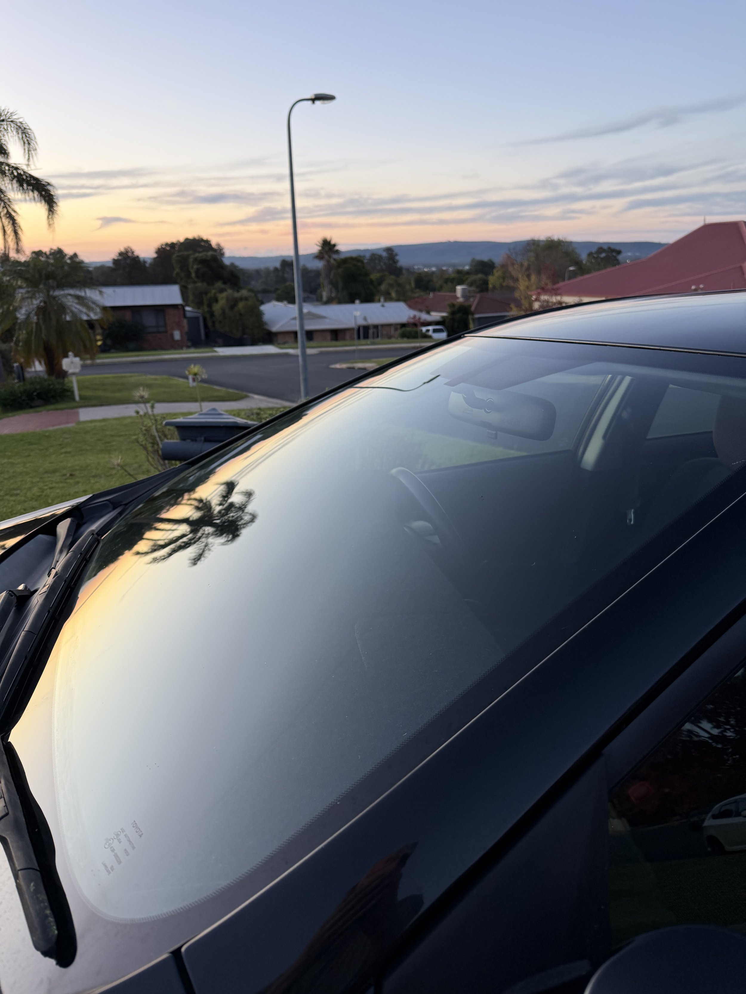 Close-up of a freshly detailed black car with a clean windscreen and glossy bonnet reflecting the sunset sky after exterior detailing.