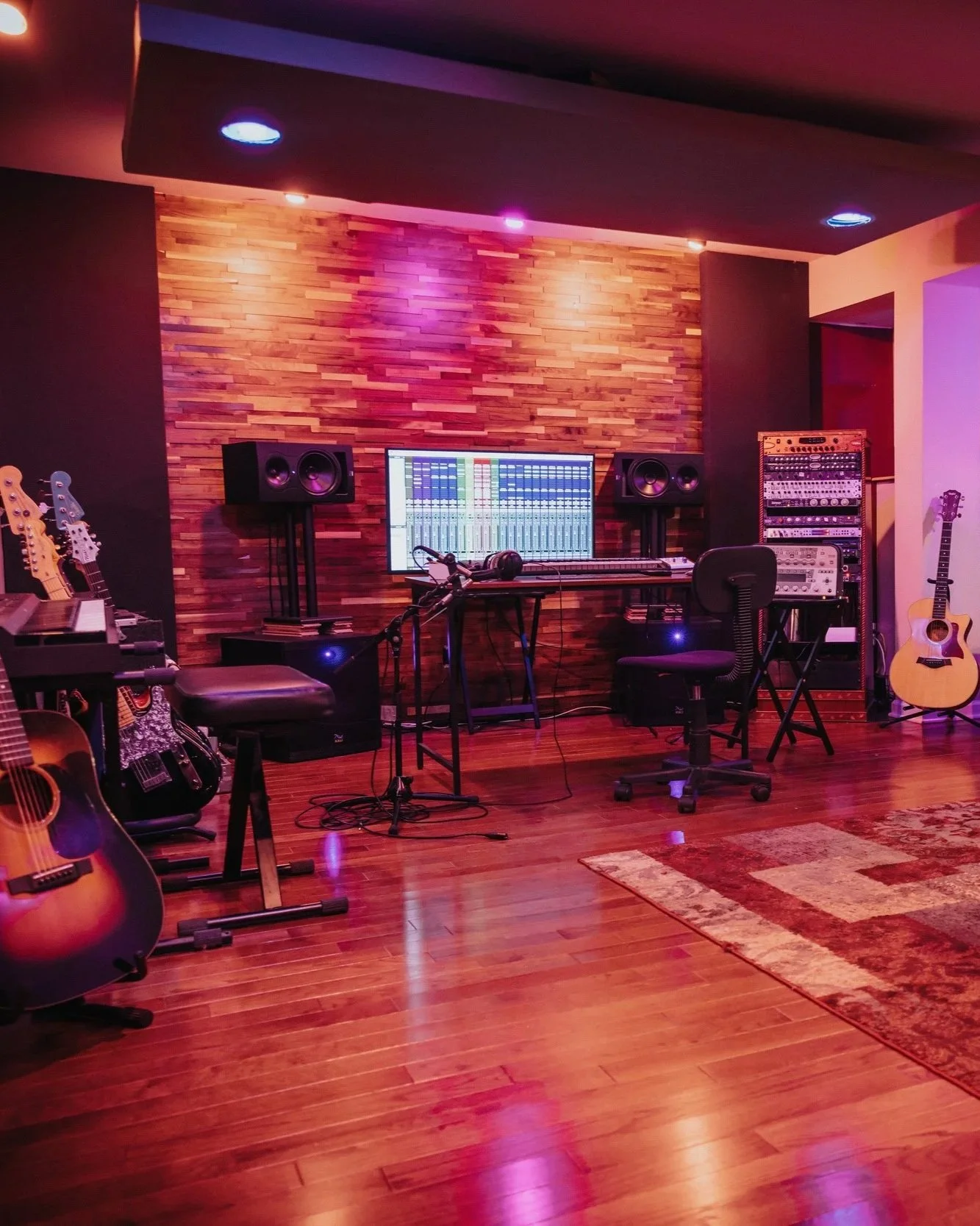 A music recording studio with guitars, a mixing console on a large screen, microphones, and various audio equipment, all set against a wooden wall background.