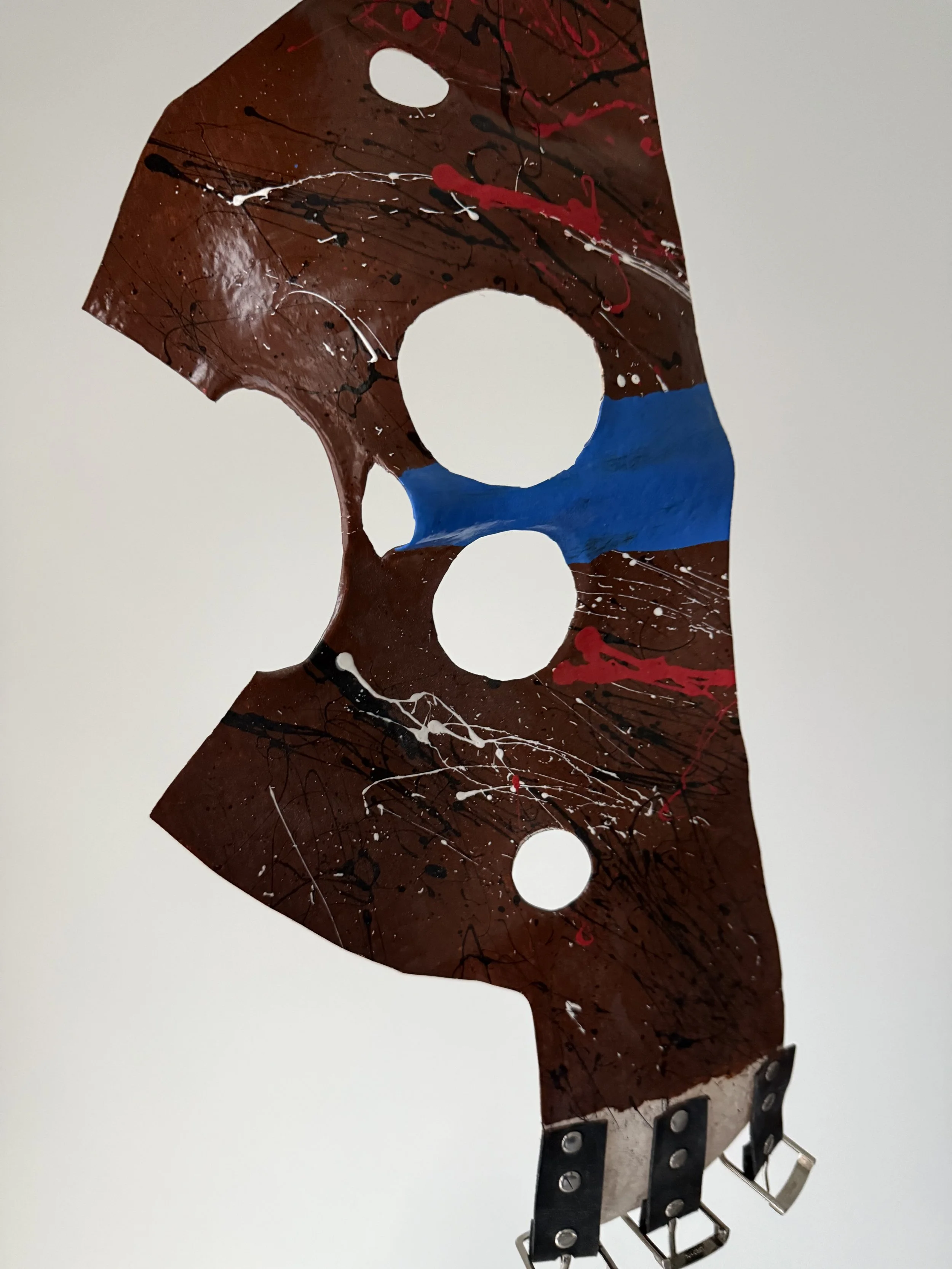 A close-up of a vintage satellite dish mounted on a wall, painted with an abstract splatter pattern in red, black, white, and blue, with a white background.