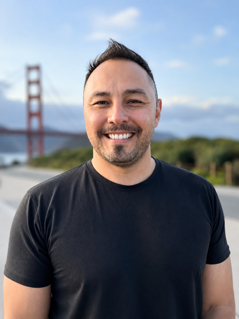 Smiling man in black T-shirt standing outdoors with the Golden Gate Bridge in the background.