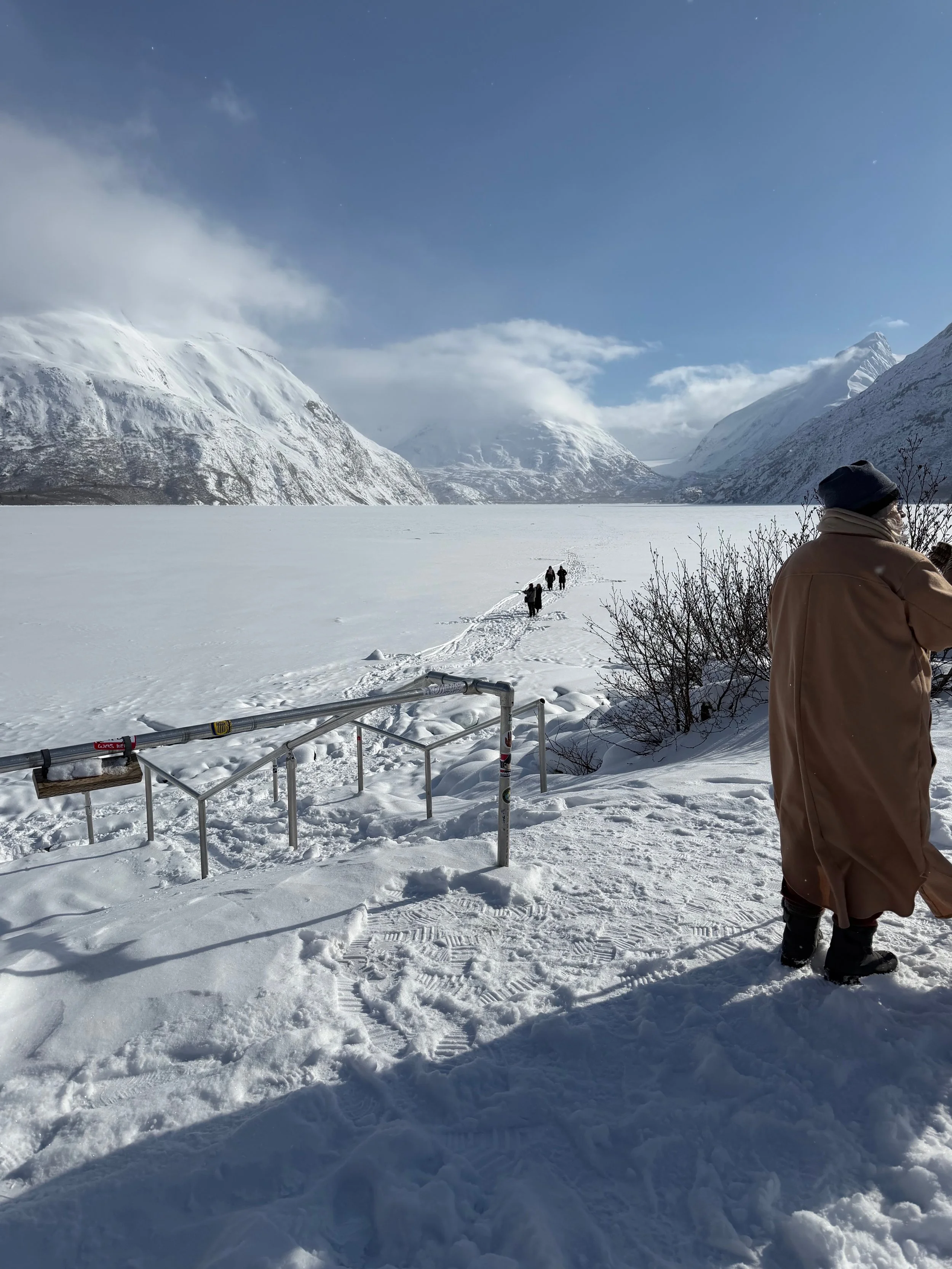 a view of mountains on the Kenai Peninsula, in Alaska. The mountains are covered with snow and artists from climate artists walk across a glacier