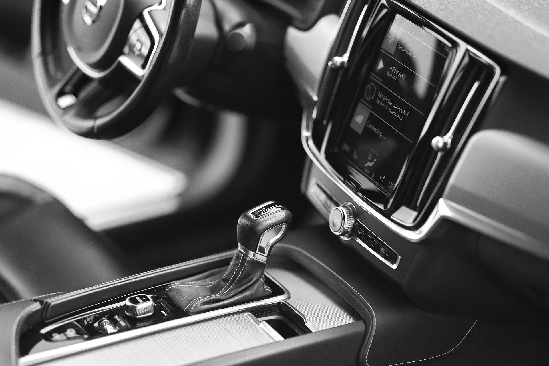 Black and white photo of a car's interior, showing the gear shift, dashboard, and a digital infotainment system.