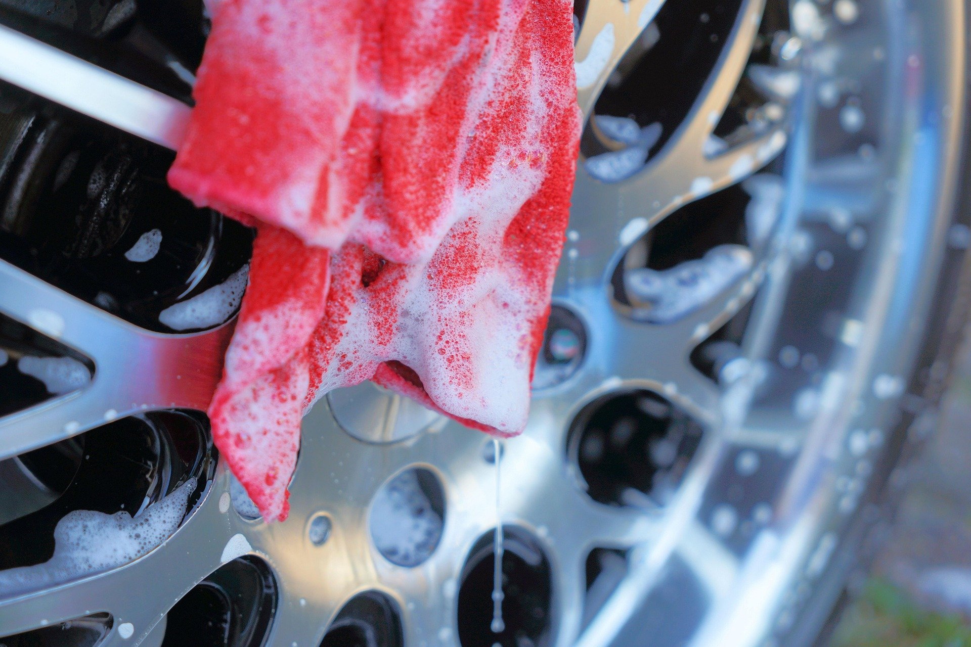 Red cleaning cloth with soap suds on a metallic bottle rack in a dishwasher