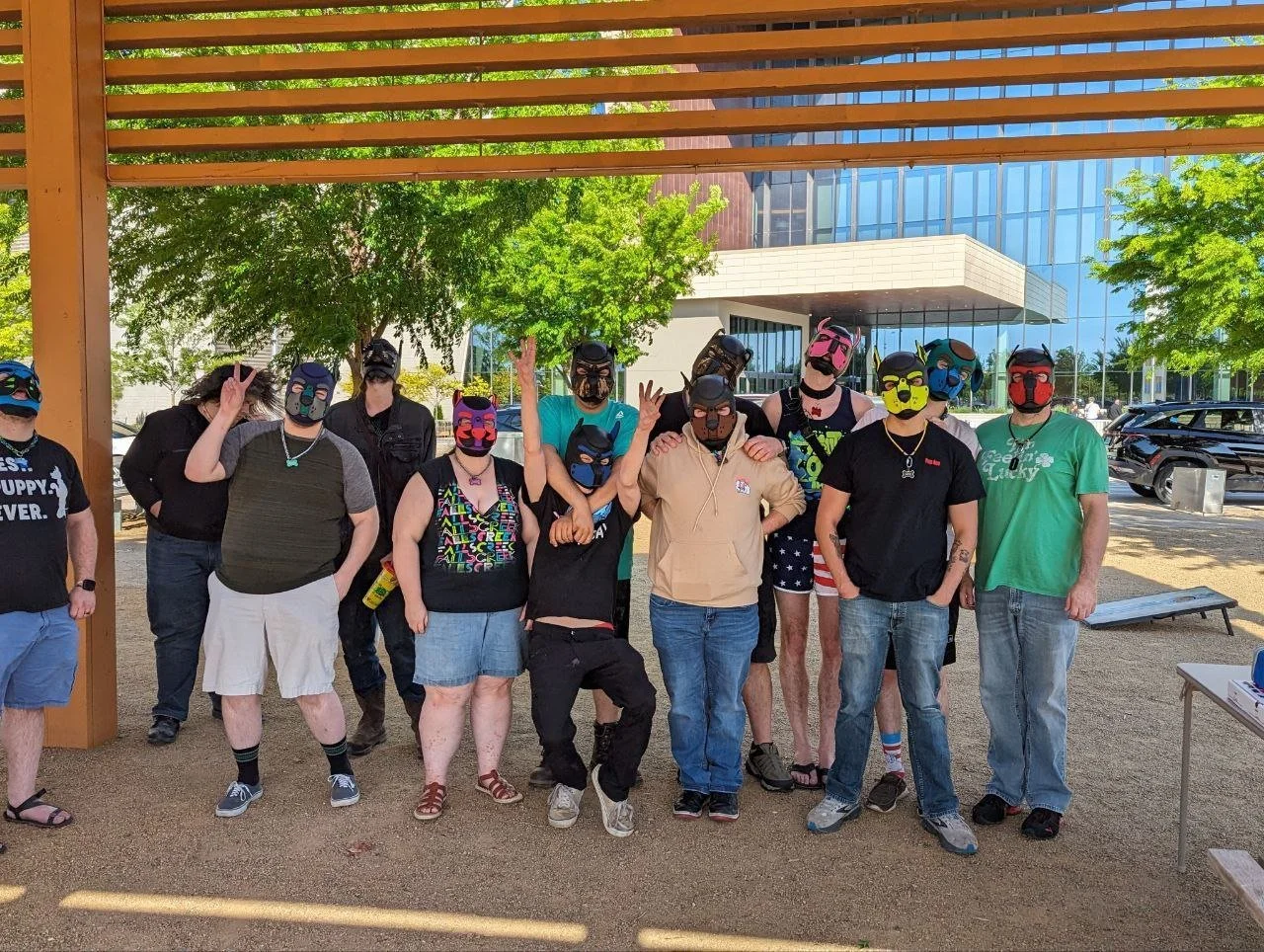 Group of people wearing colorful masks standing outdoors on a sunny day near modern buildings and trees.