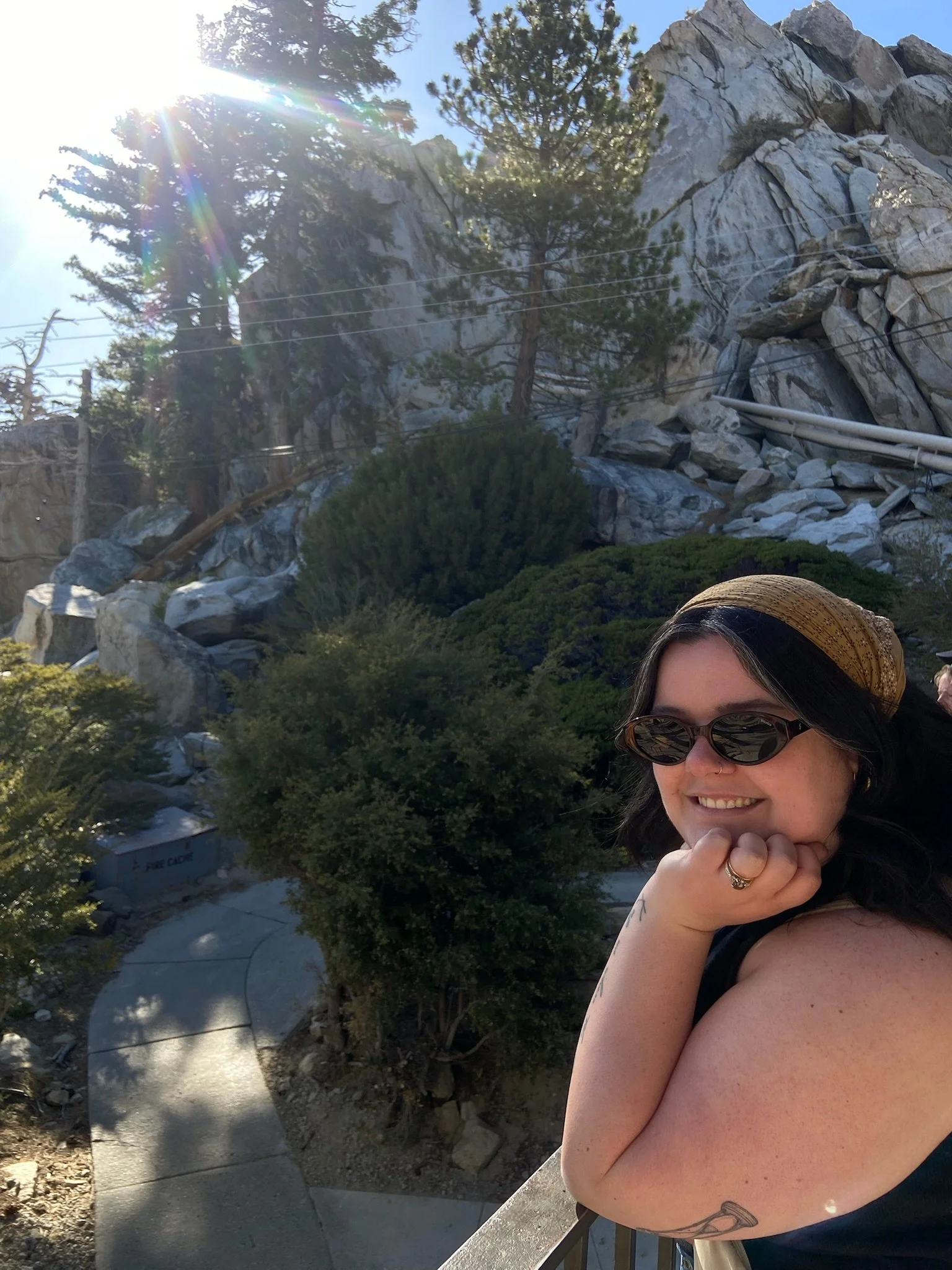 Photo of woman standing in front of mountains and trees with sun spot coming in from the side