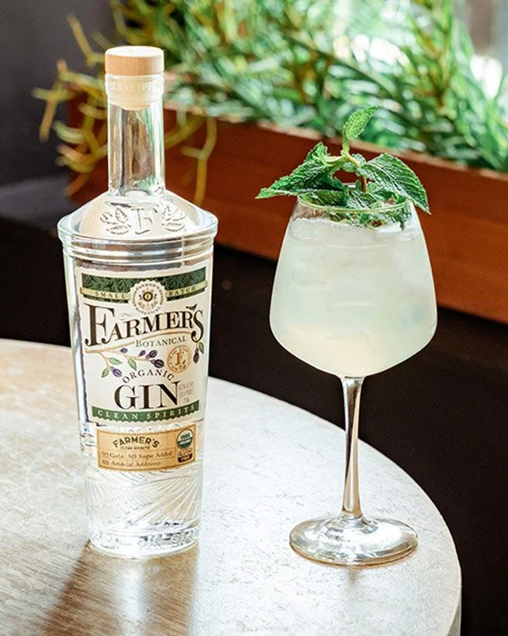 Botella de ginebra orgánica Farmer's y un cóctel con menta y hielo en un vaso de copa en una mesa de madera