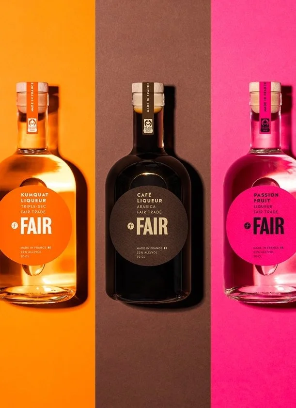 Tres botellas de licor con etiquetas de colores naranja, negro y rosa, colocadas sobre fondos de colores a juego: naranja, marrón y rosa.