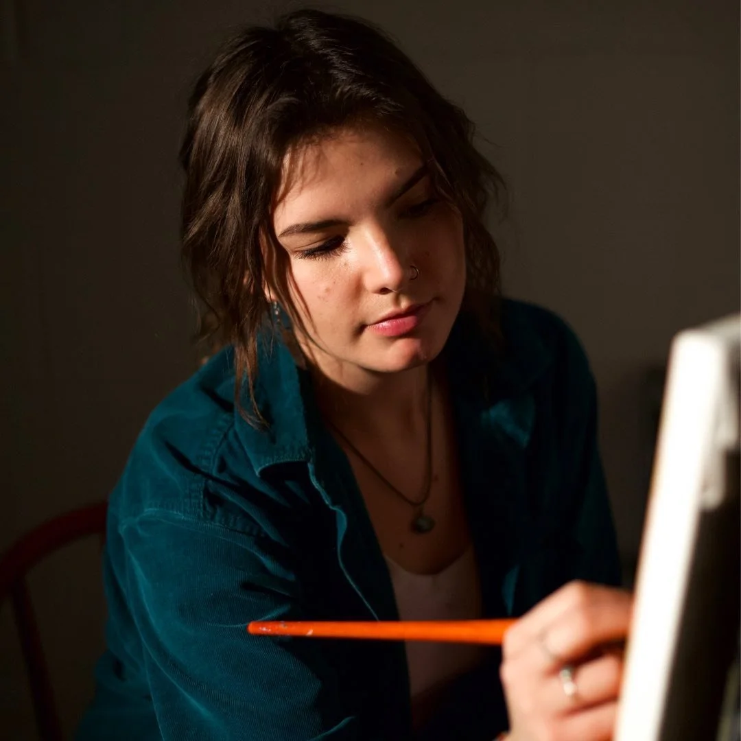 Portrait of artist Sierra Kowalski painting in a softly lit studio setting