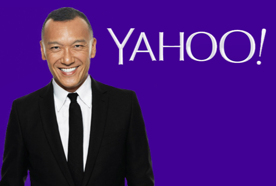 A man in a black suit and tie smiling against a purple background with the Yahoo! logo.