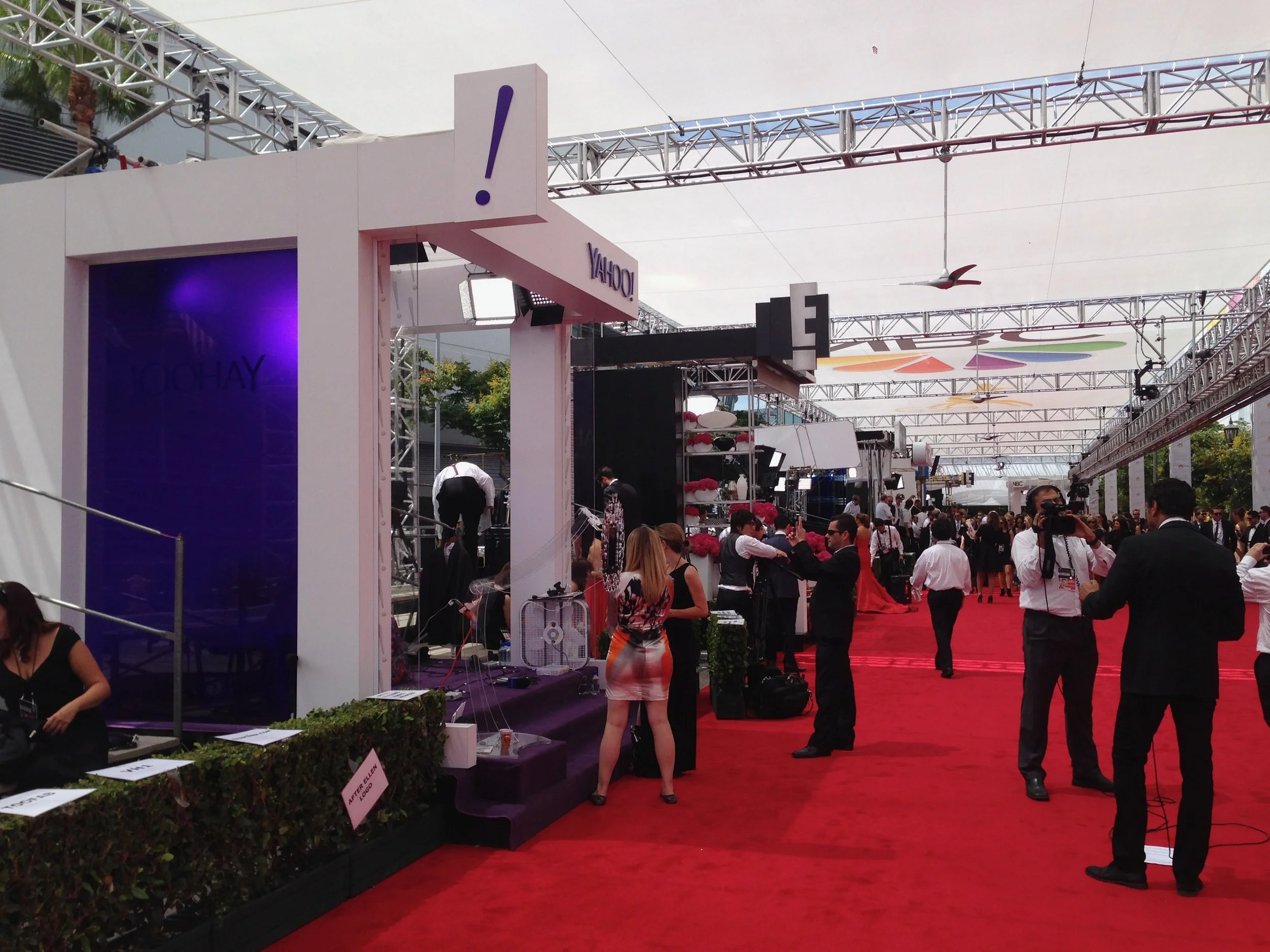 A crowded exhibition area with booths and a red carpet, with people mingling and taking photos.