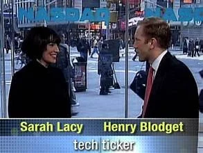 A woman and a man talking in a television studio, with a city street visible through large outdoor windows in the background. The on-screen text shows Sarah Lacy and Henry Blodget, with the caption 'tech ticker'.