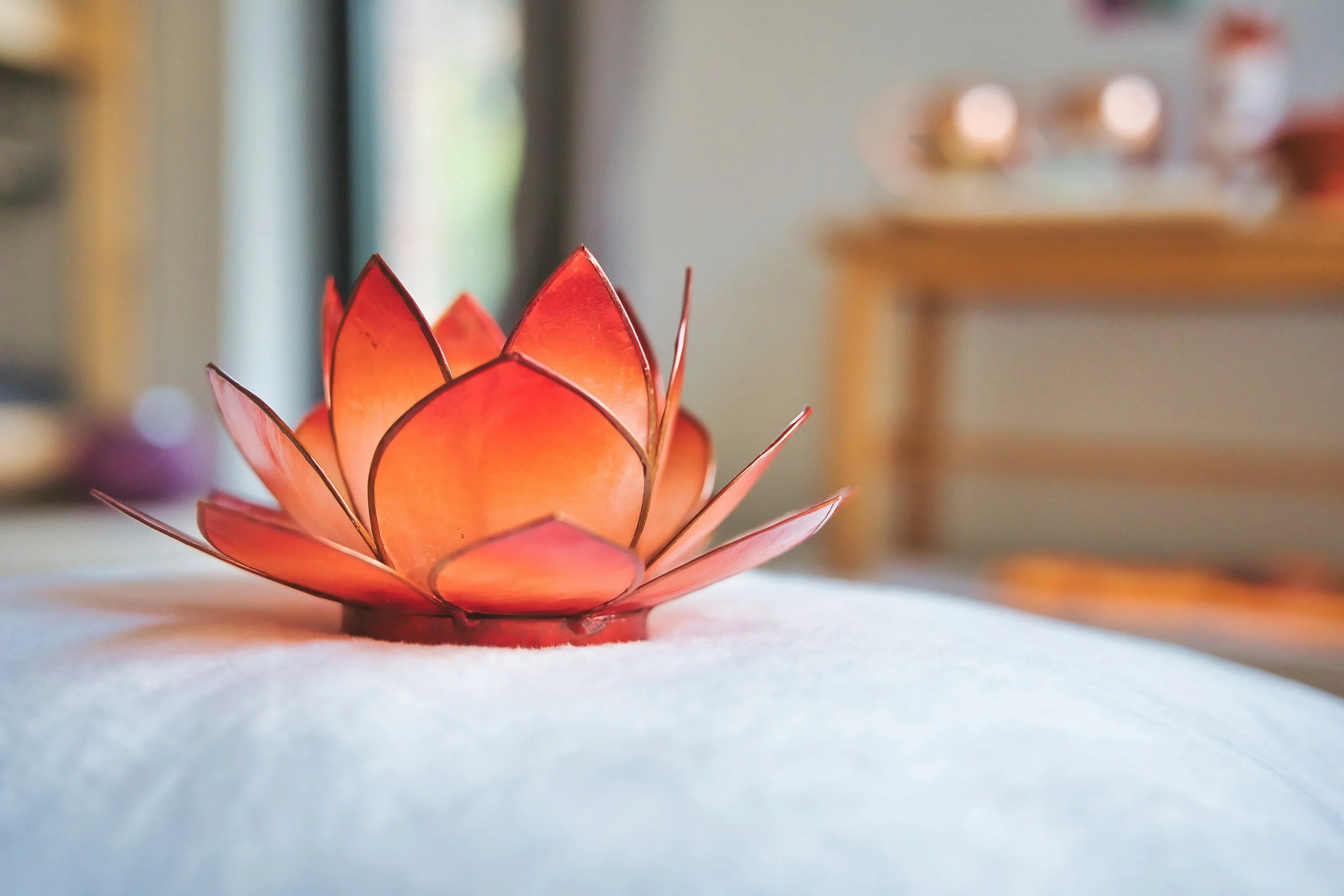A glowing, decorative lotus-shaped candle or lantern made of red and orange glass resting on a white surface in indoor lighting.