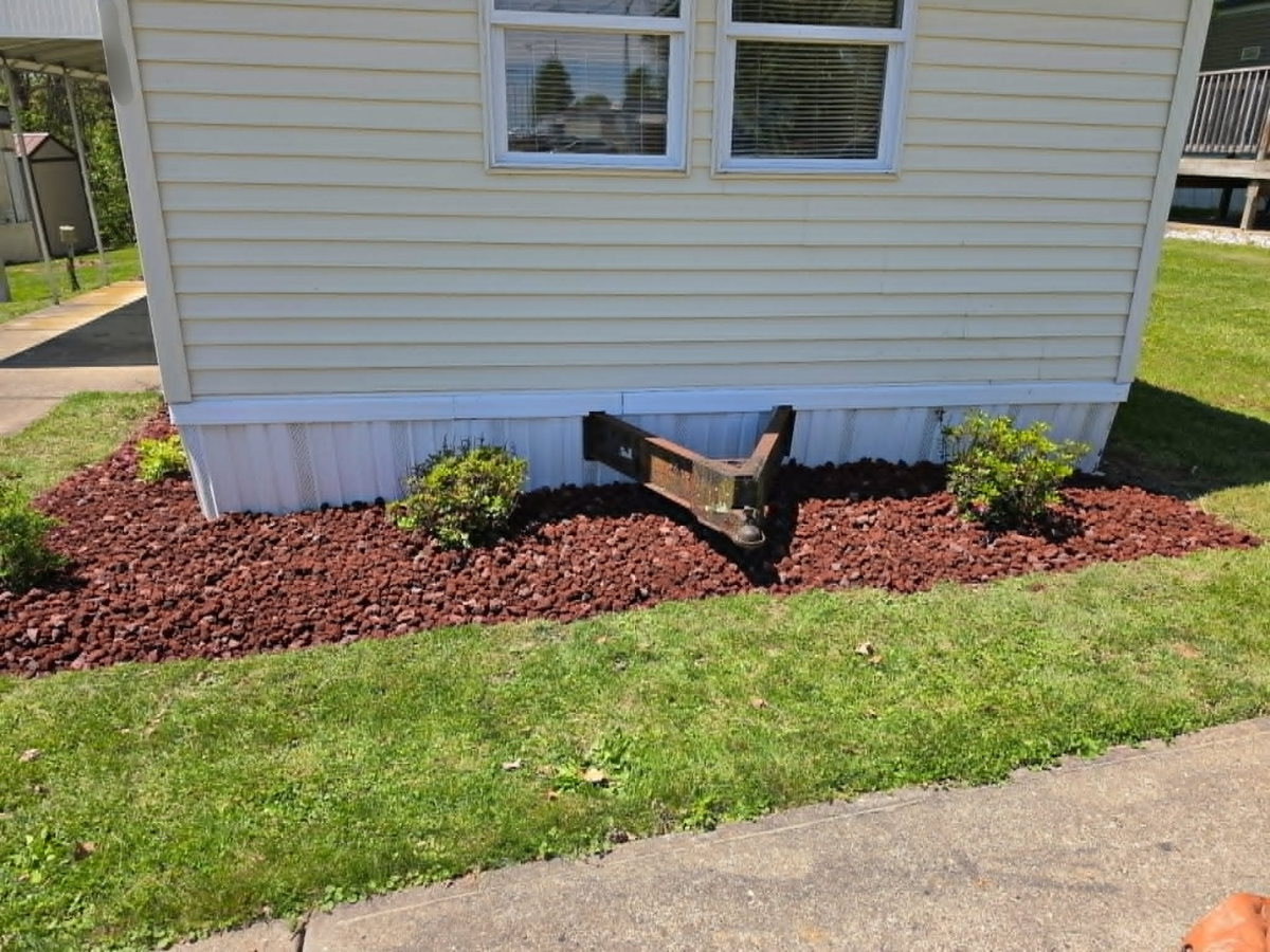 Front view of a house with flowerbed, two small shrubs, and a wooden frame for a future planting bed in the flowerbed.