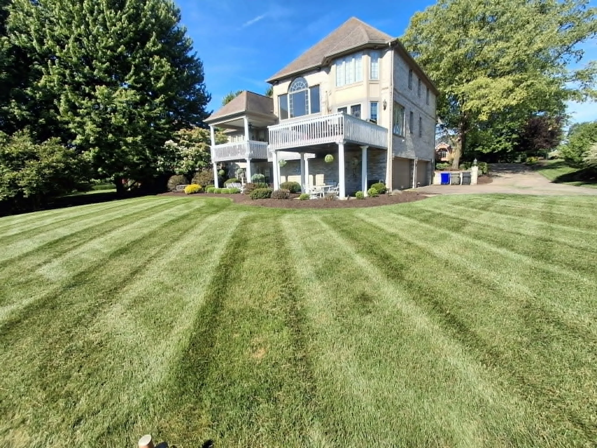 A large, well-maintained grassy backyard with a house in the background surrounded by trees.