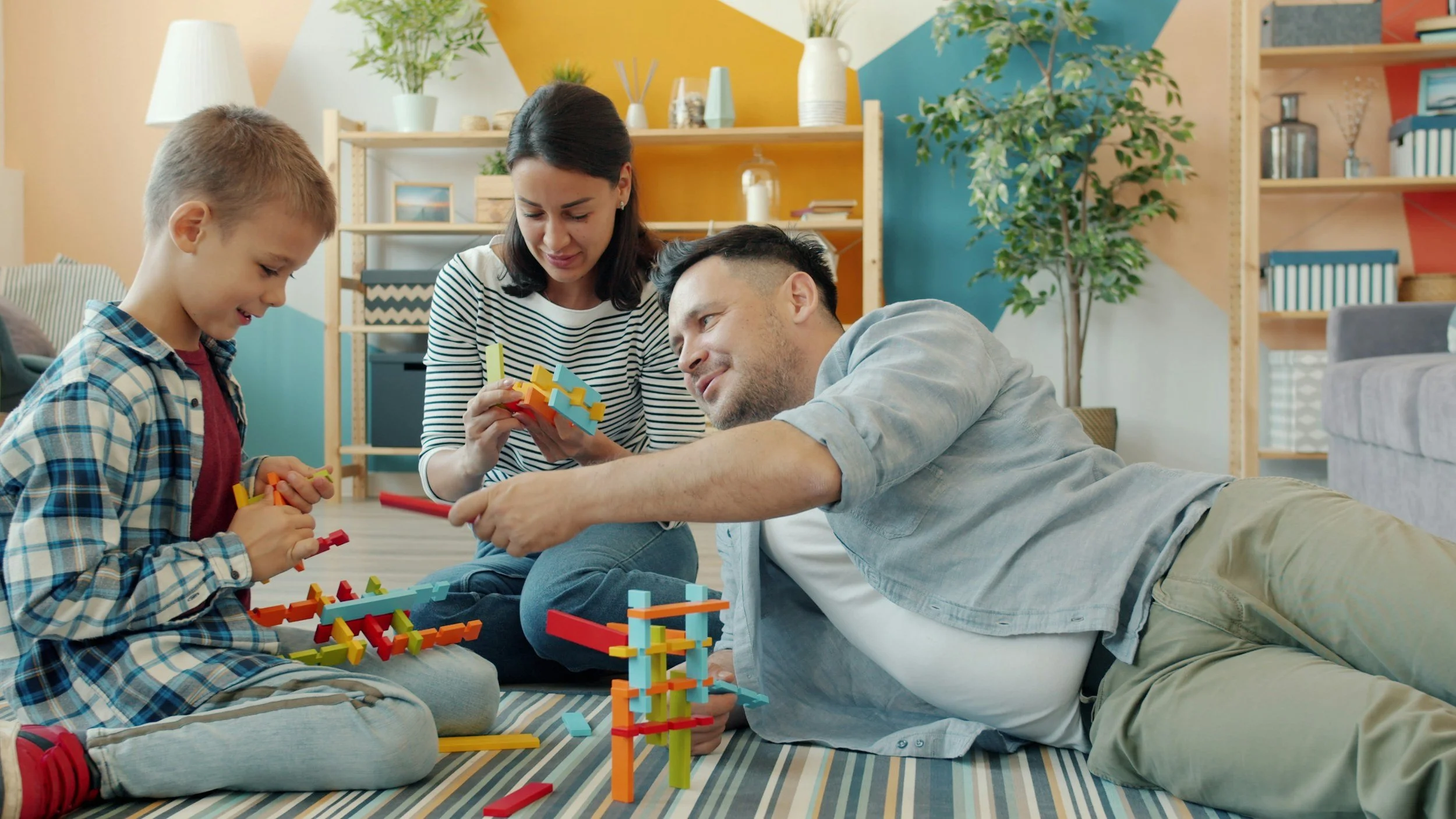 Family playing with colorful building blocks on a striped rug in a cozy living room.