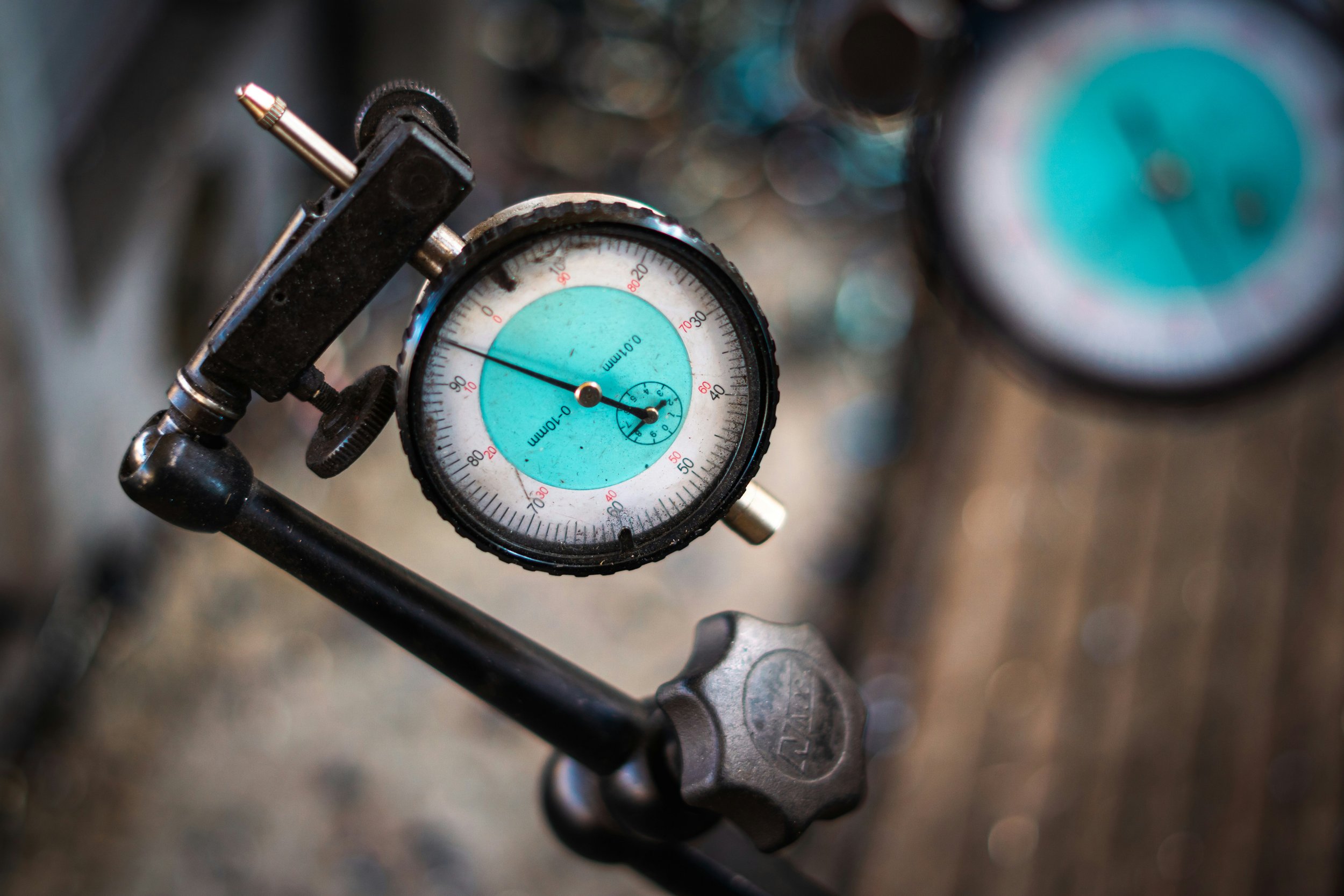 Close-up of a pressure gauge with a black dial and a turquoise background surrounded by metal and mechanical parts.
