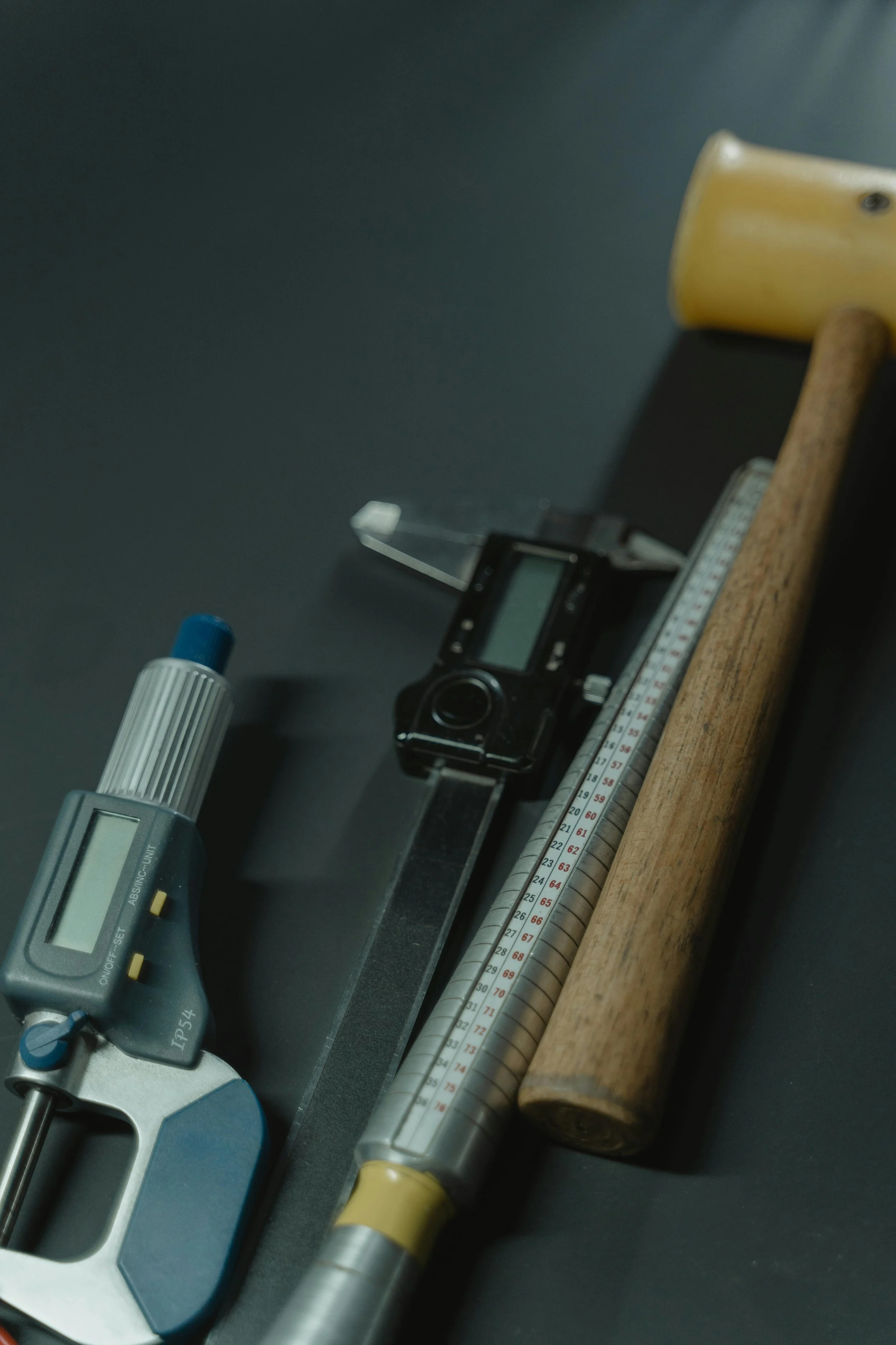 Close-up of laboratory equipment including a digital pipette, a thermometer, a small digital device, and a wooden stick, set against a dark background.